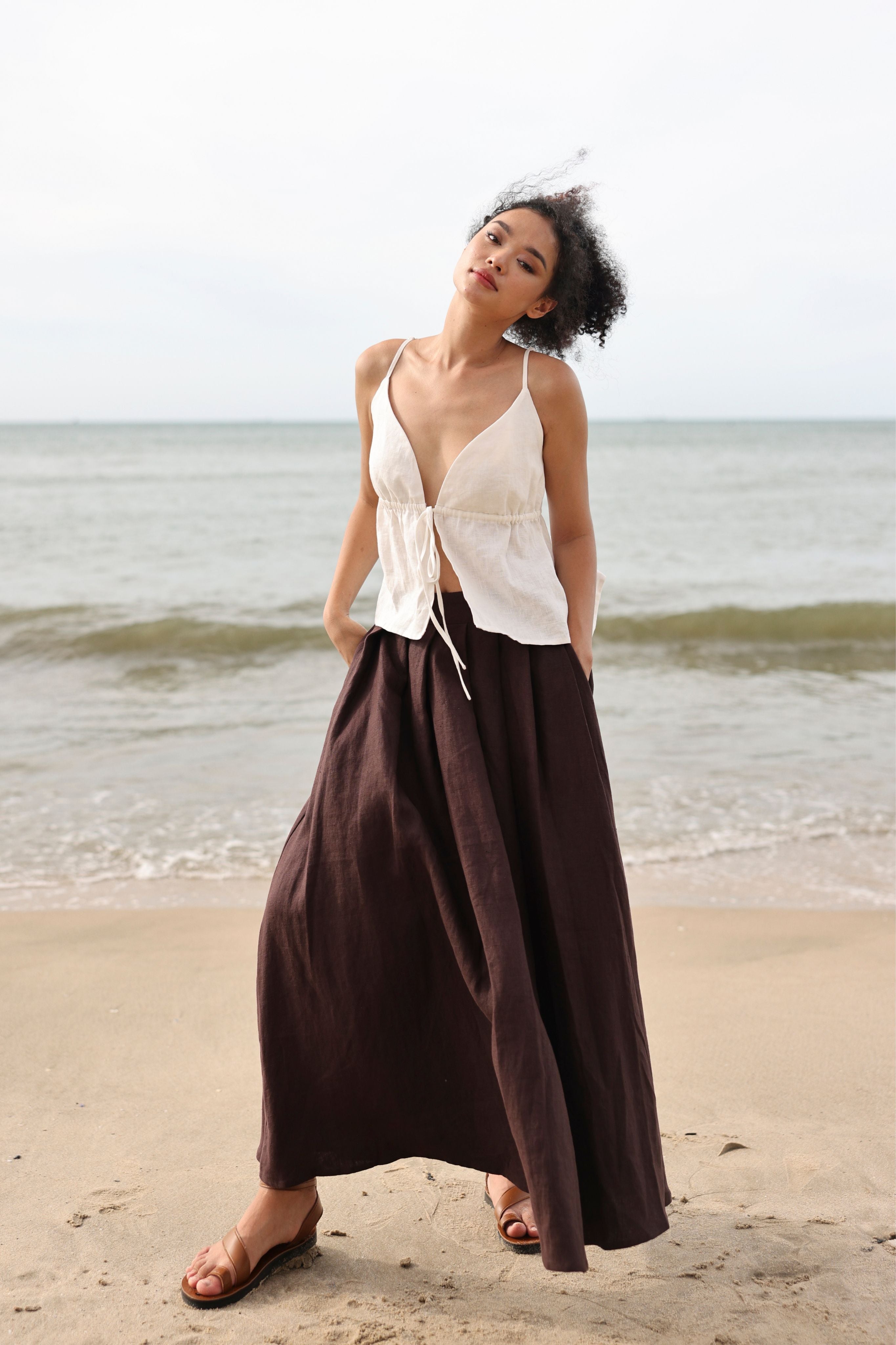 Woman in a white top and brown skirt standing on a beach.