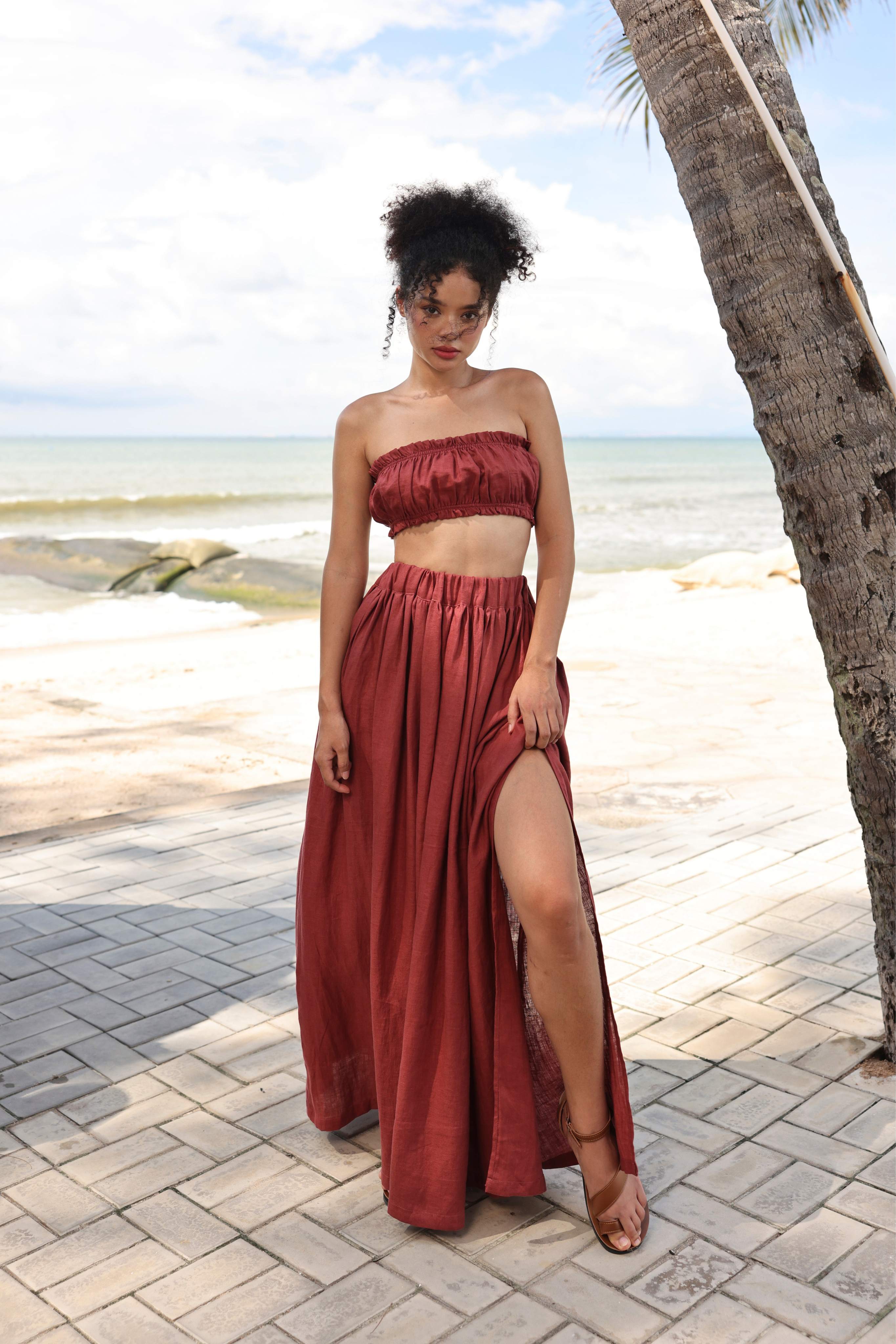 Woman in a red strapless top and long skirt standing on a beach path with palm trees.