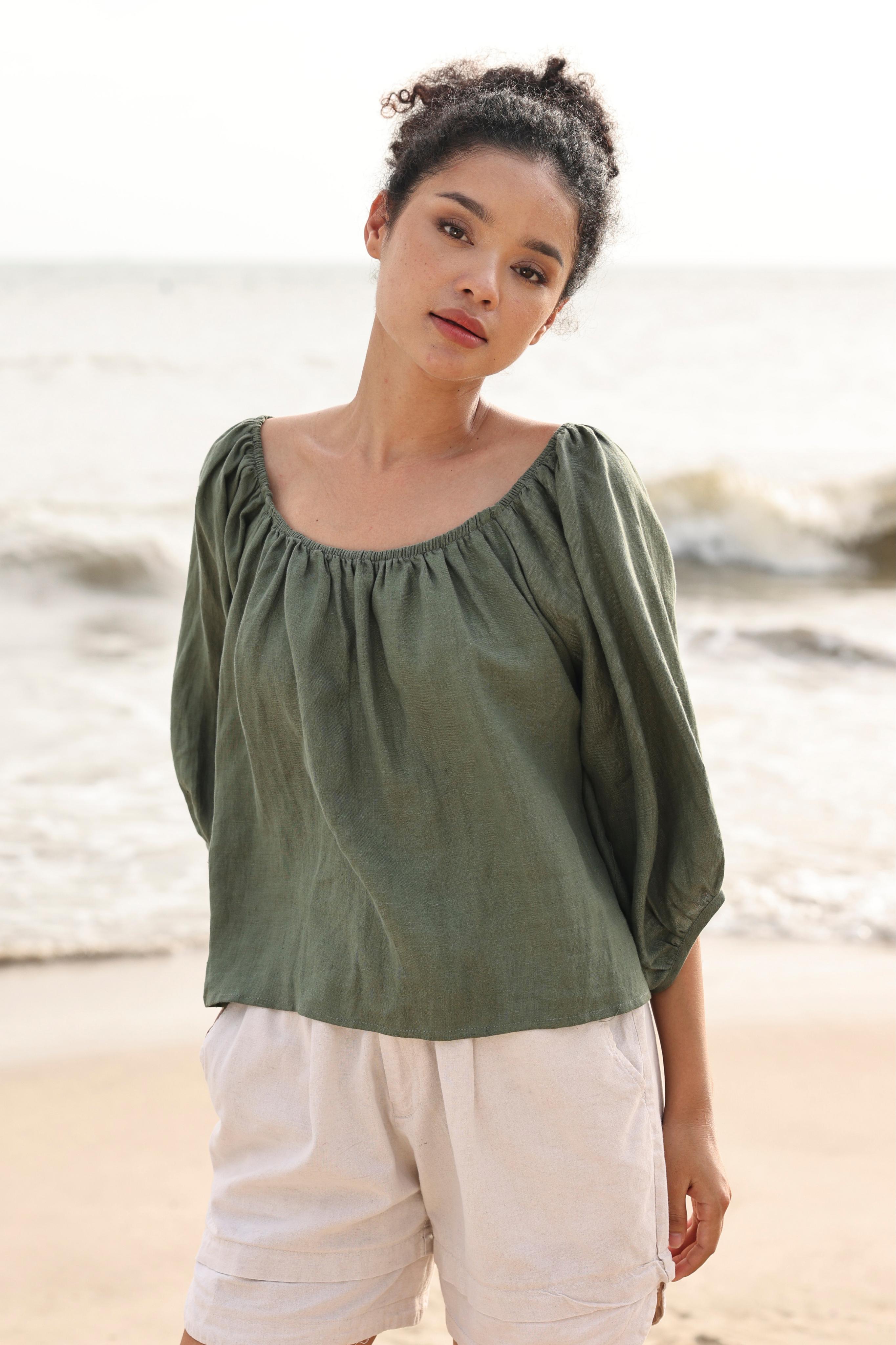 Woman wearing a green top and white pants standing on a beach.