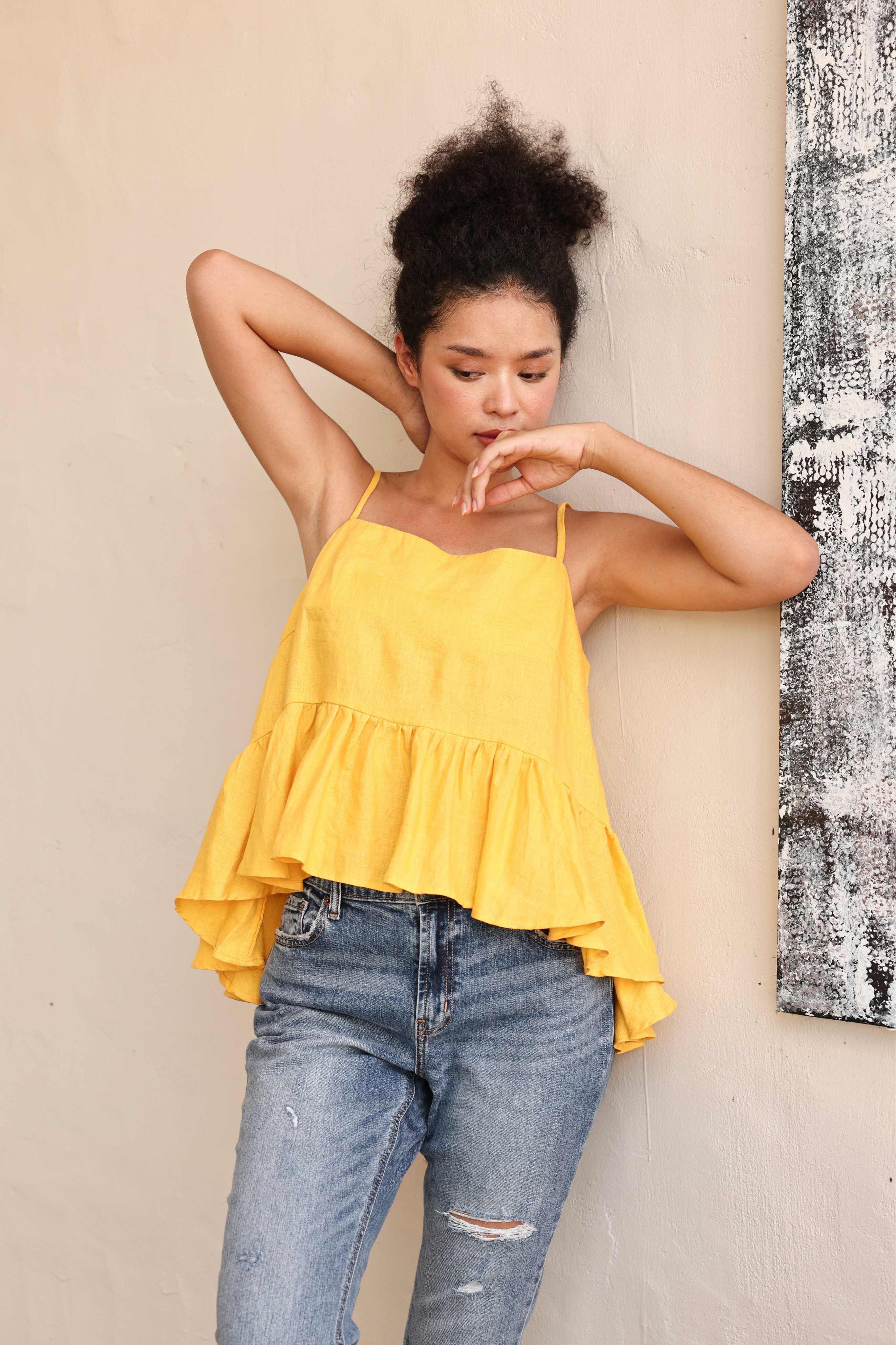 Woman wearing a yellow top and blue jeans against a beige wall.