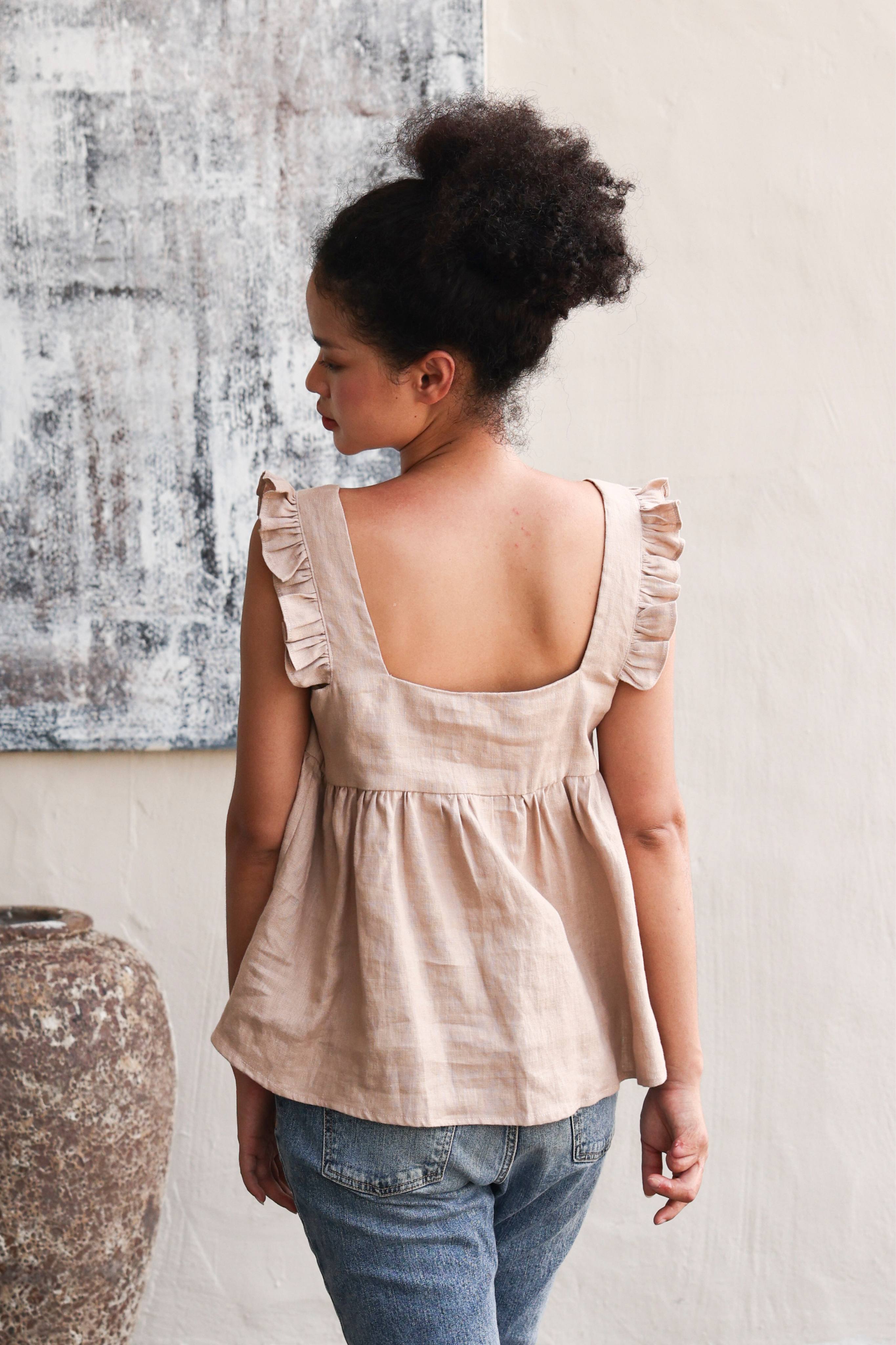 Woman wearing a top with ruffled sleeves and blue jeans, standing against a textured wall.