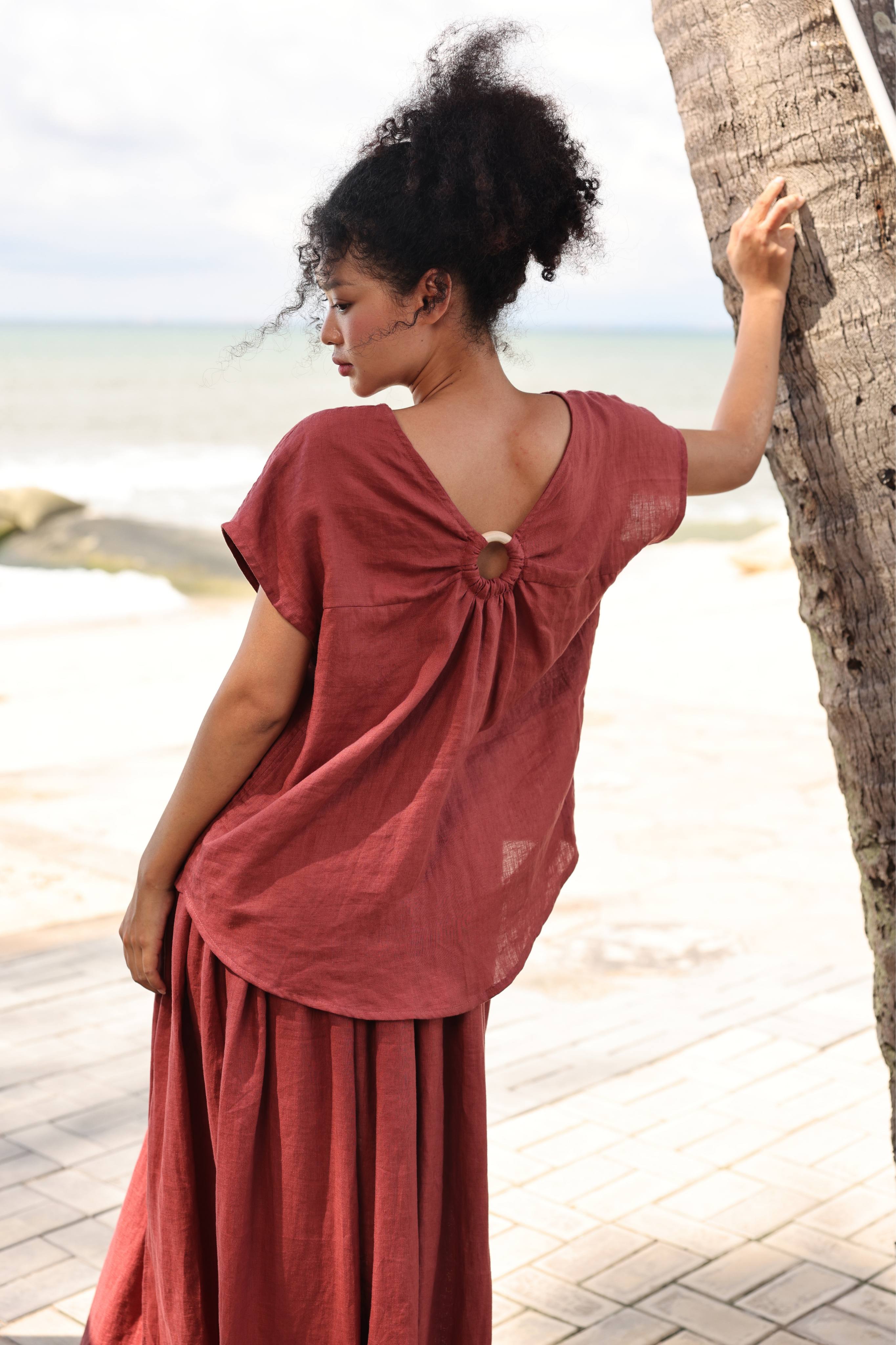 Woman in a rust-colored top standing by a palm tree on a beach.