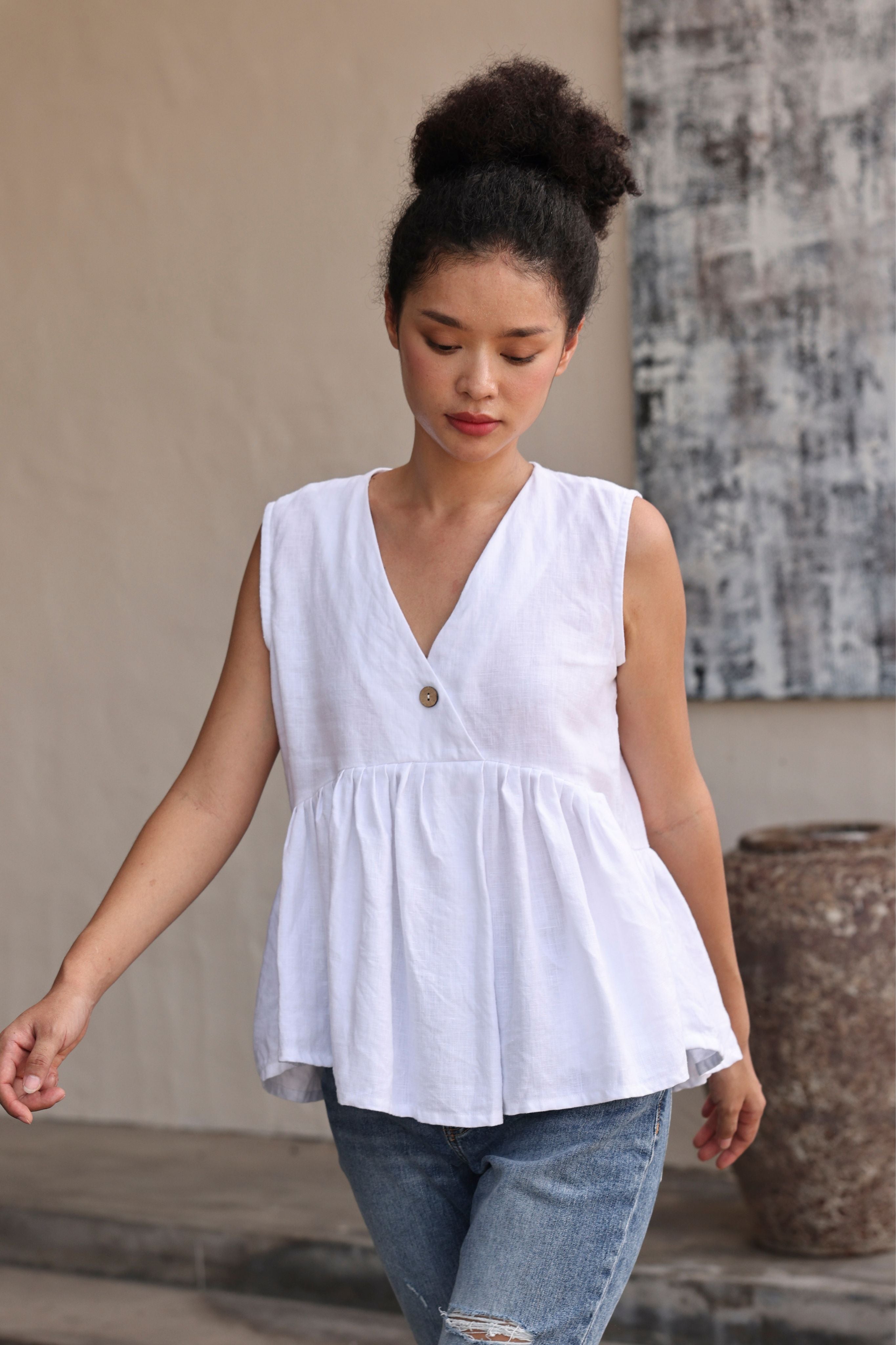 Woman wearing a white sleeveless top with a button detail, standing outdoors.