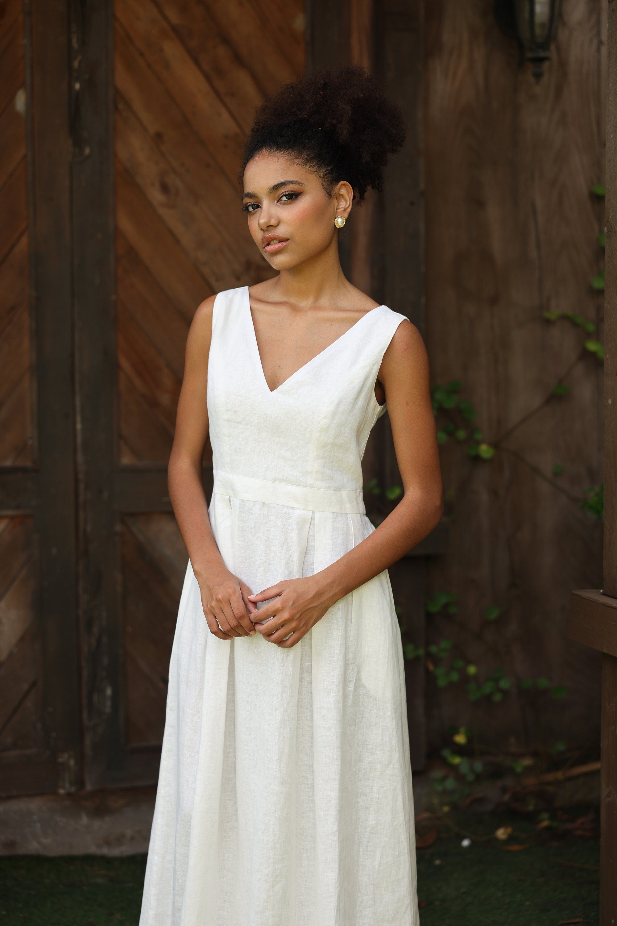 Woman in an ivory dress standing against a wooden wall.