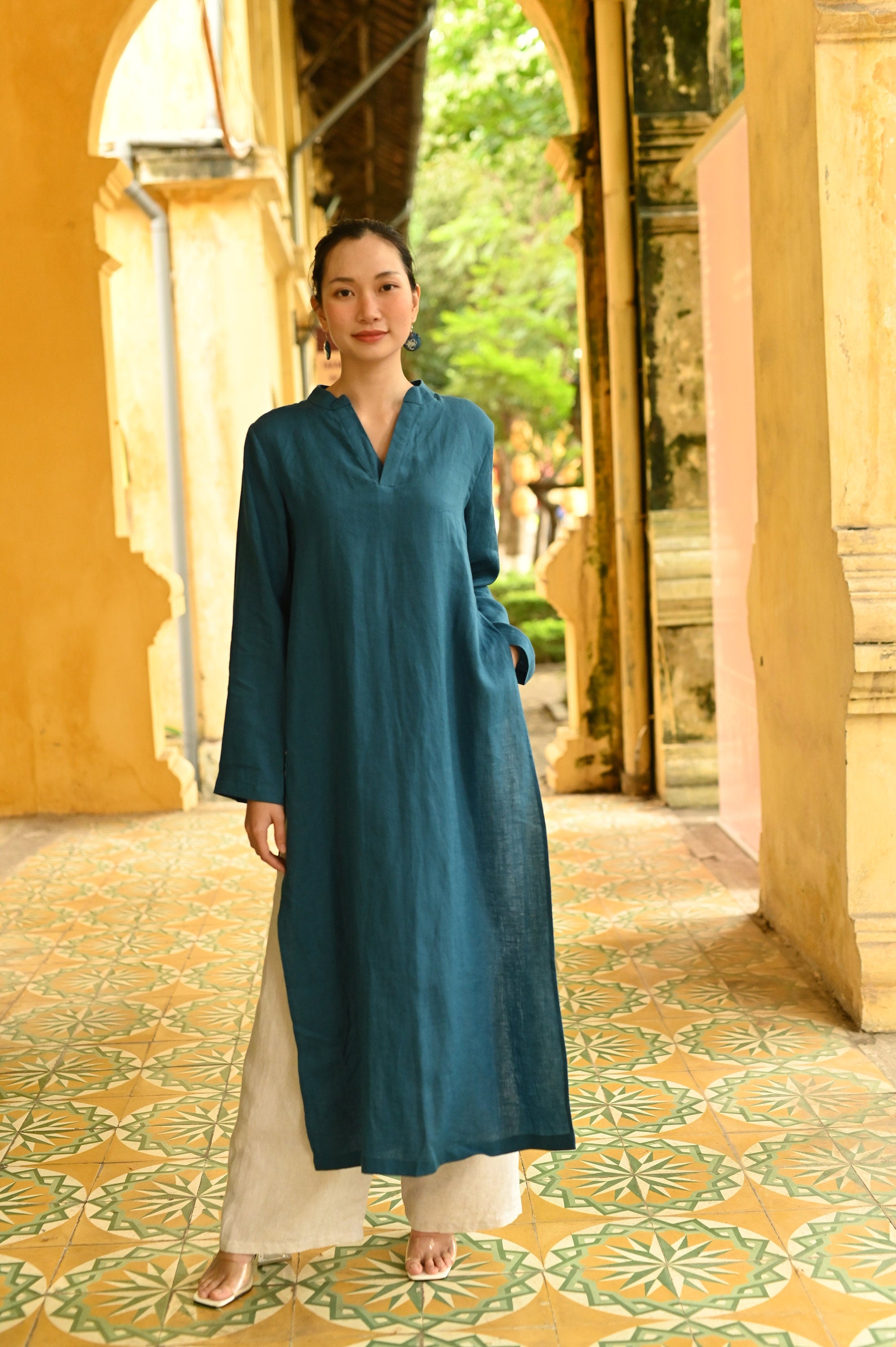 Woman in a teal tunic standing in a decorative outdoor setting with arches and patterned floor.