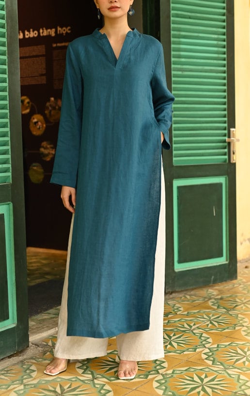 Person wearing a teal long dress standing in front of green doors with a patterned floor.