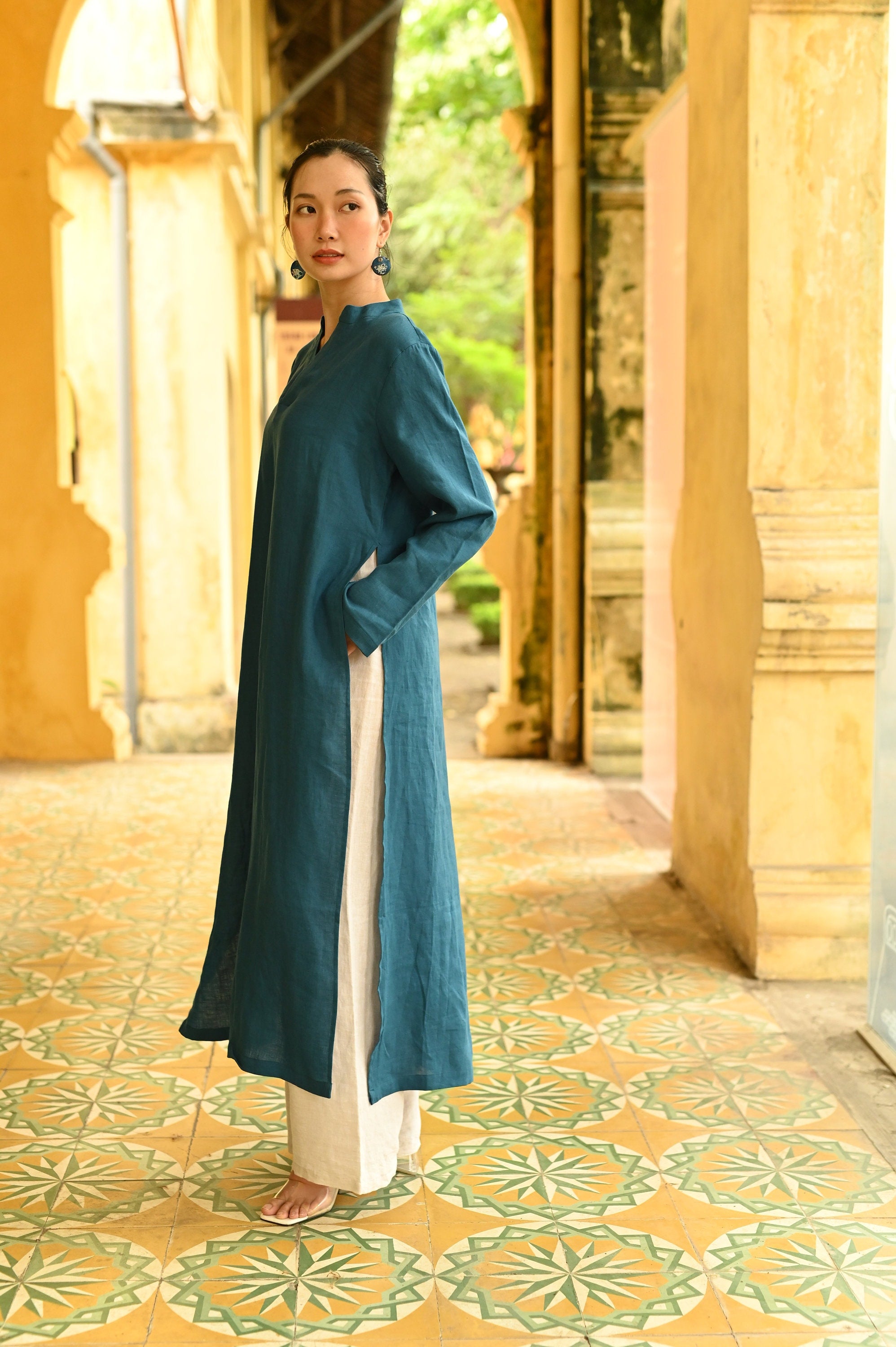 Woman in a teal dress standing in an outdoor setting with architectural columns and greenery.