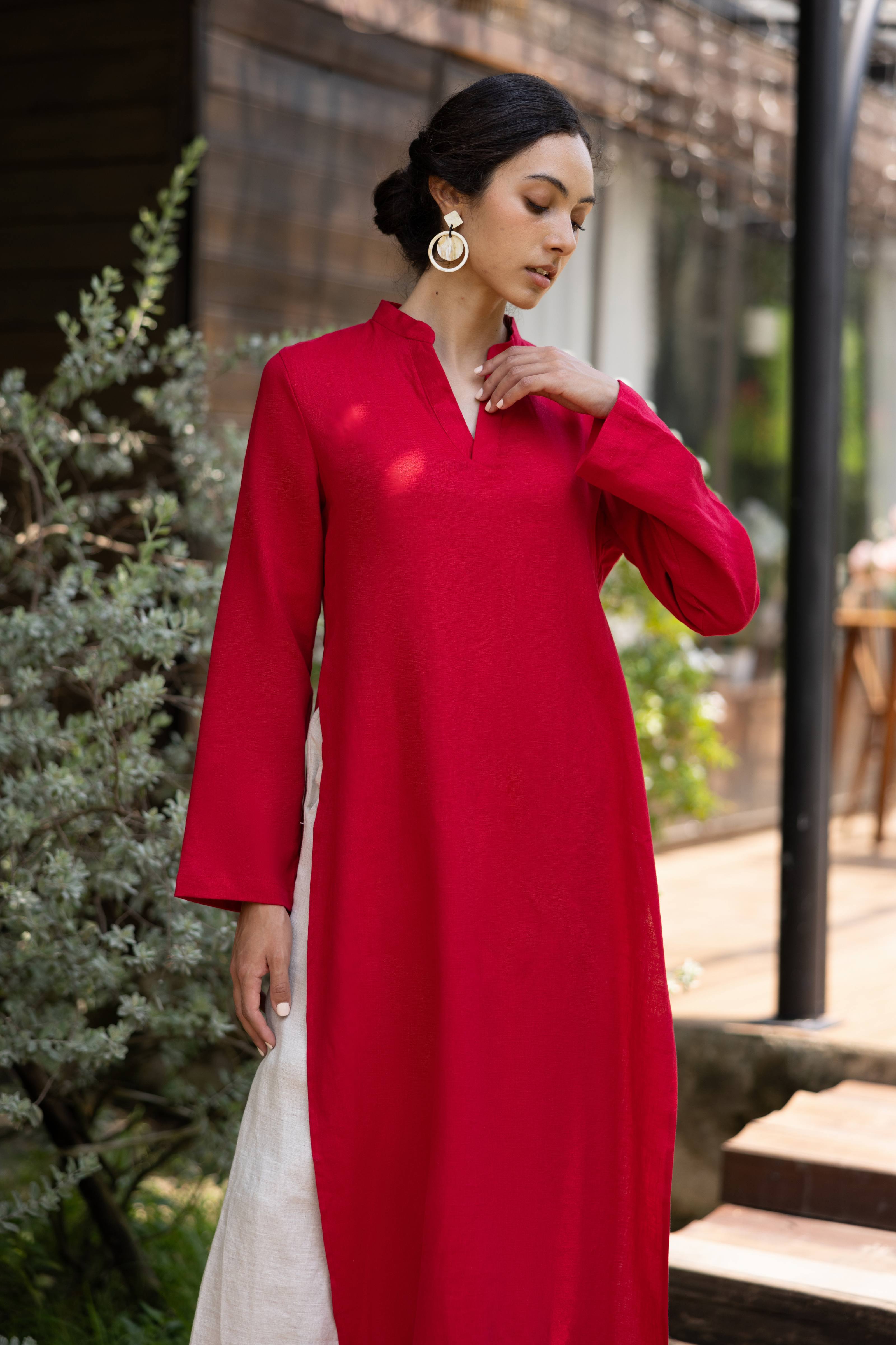 Woman wearing a red dress standing outdoors with greenery in the background