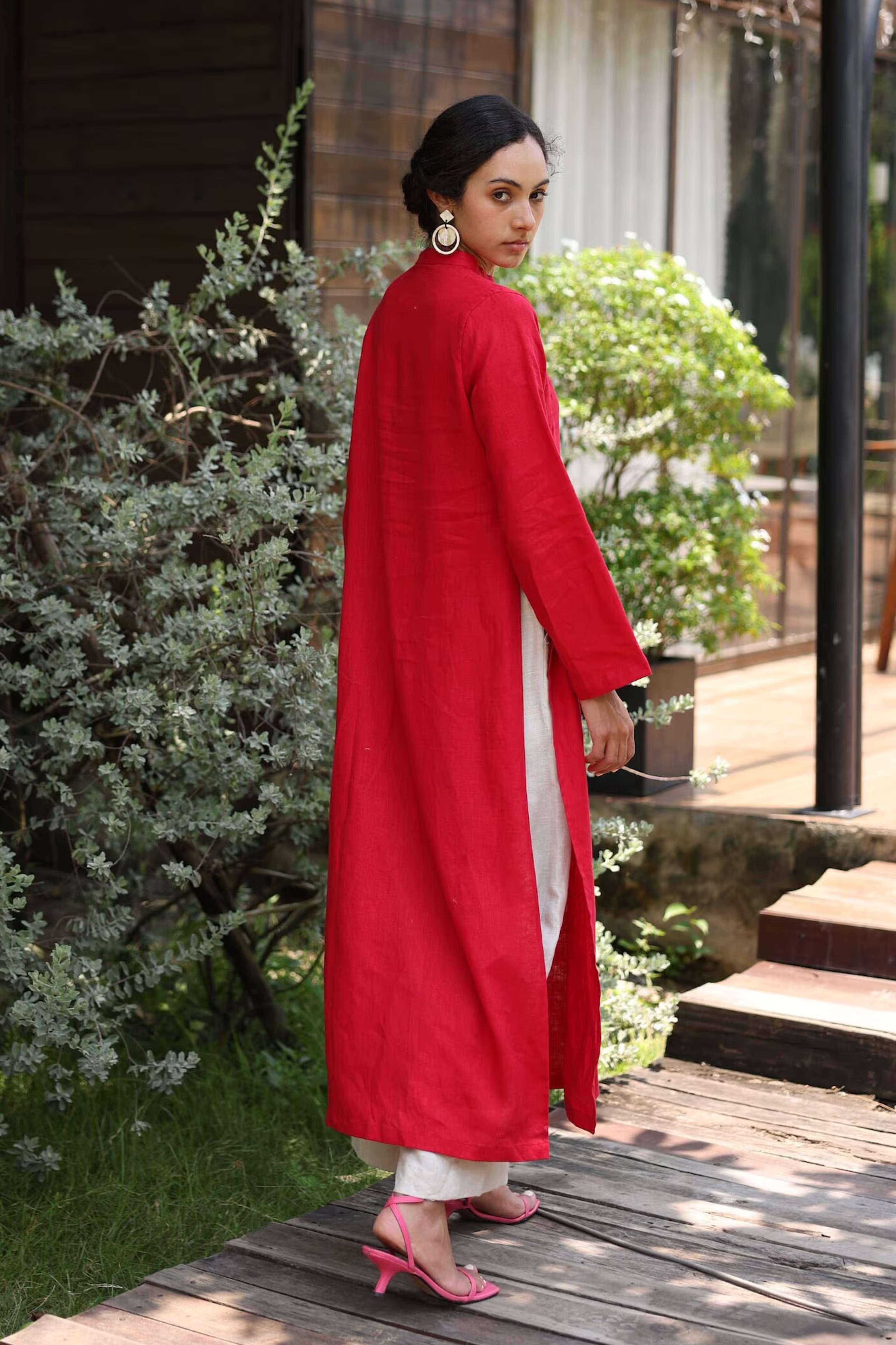 Woman wearing a red long tunic in an outdoor setting with plants and steps.