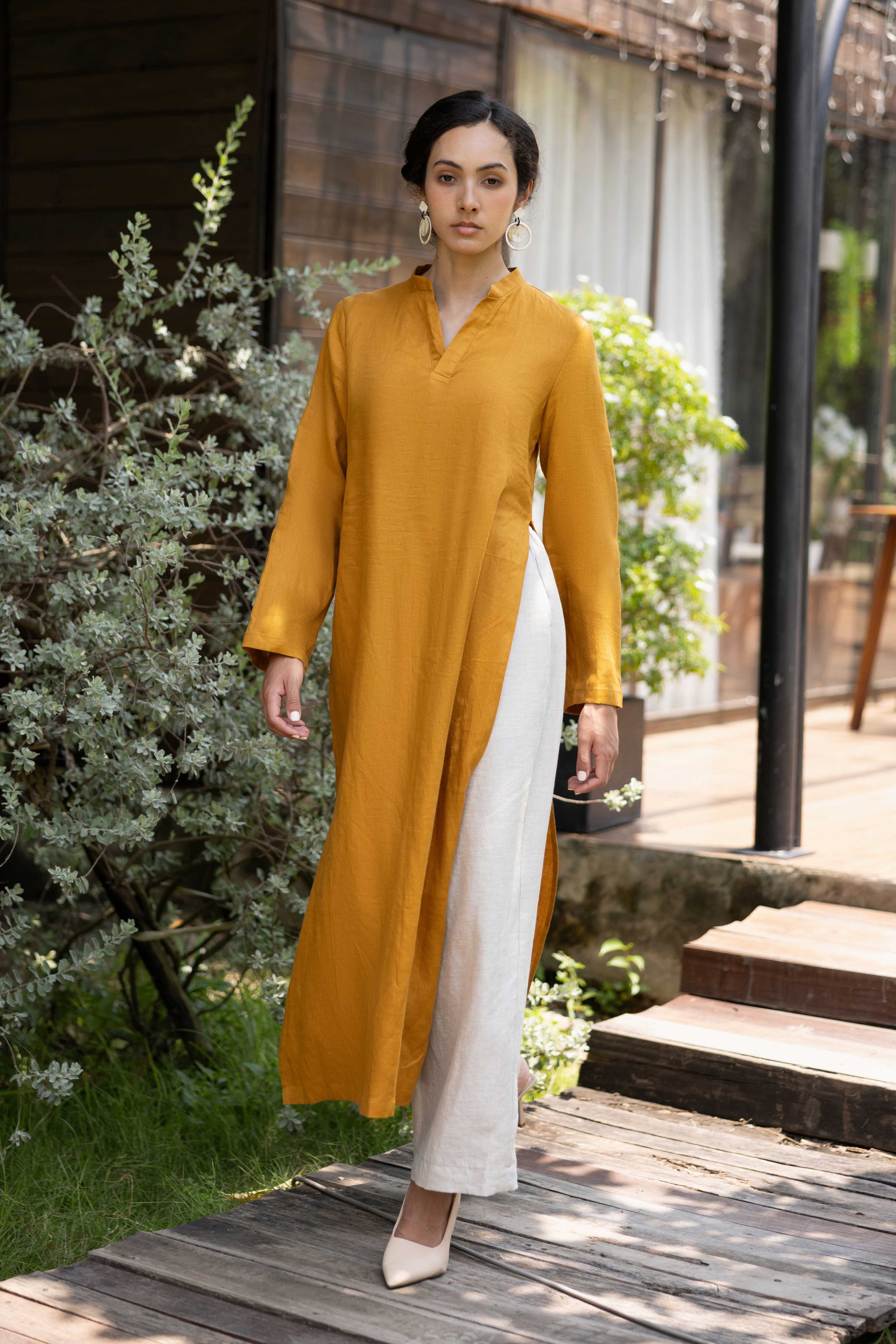 Woman wearing a mustard yellow kurta with white pants standing outdoors.