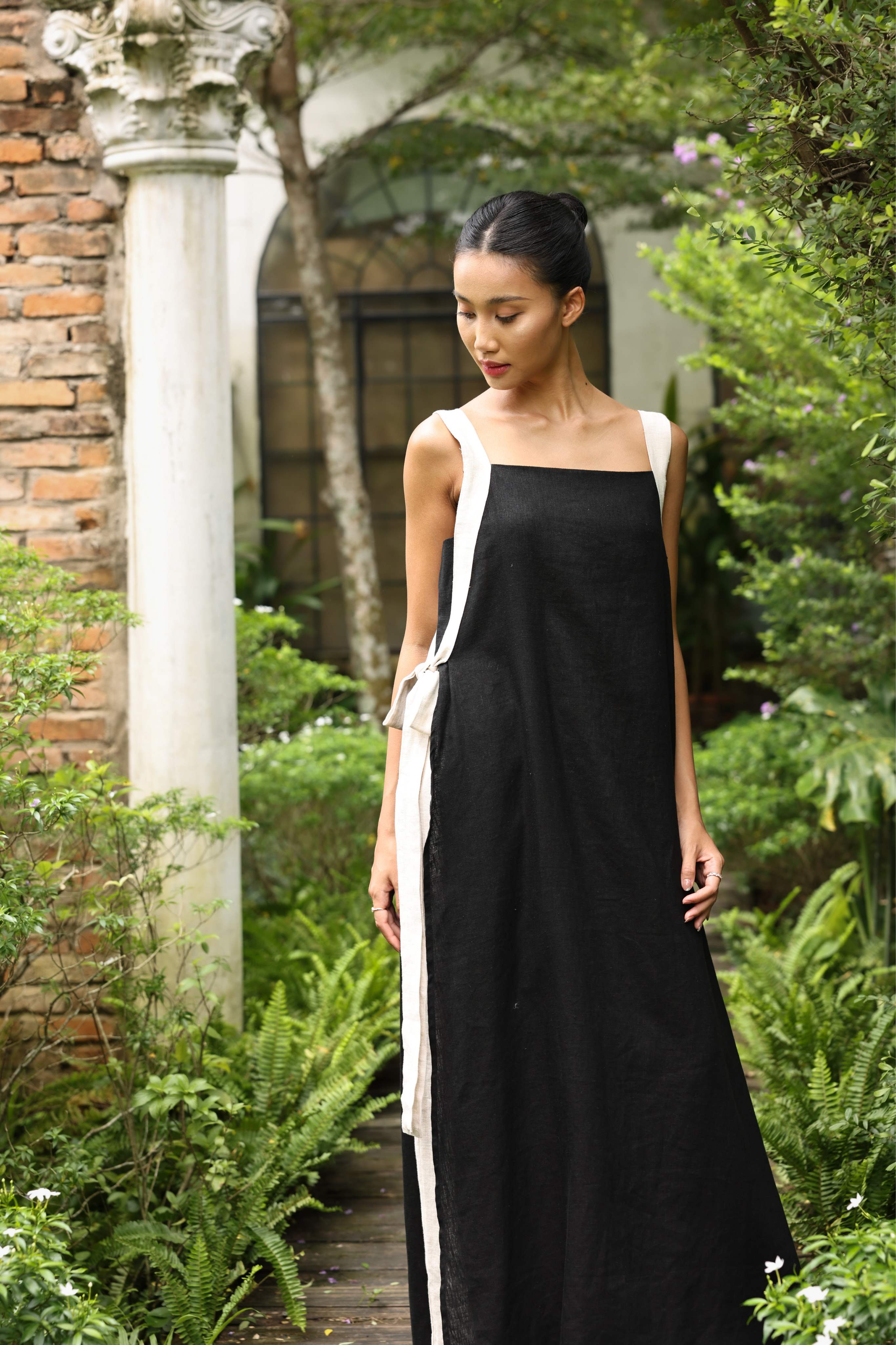 Woman wearing a black dress with white trim standing in a garden.