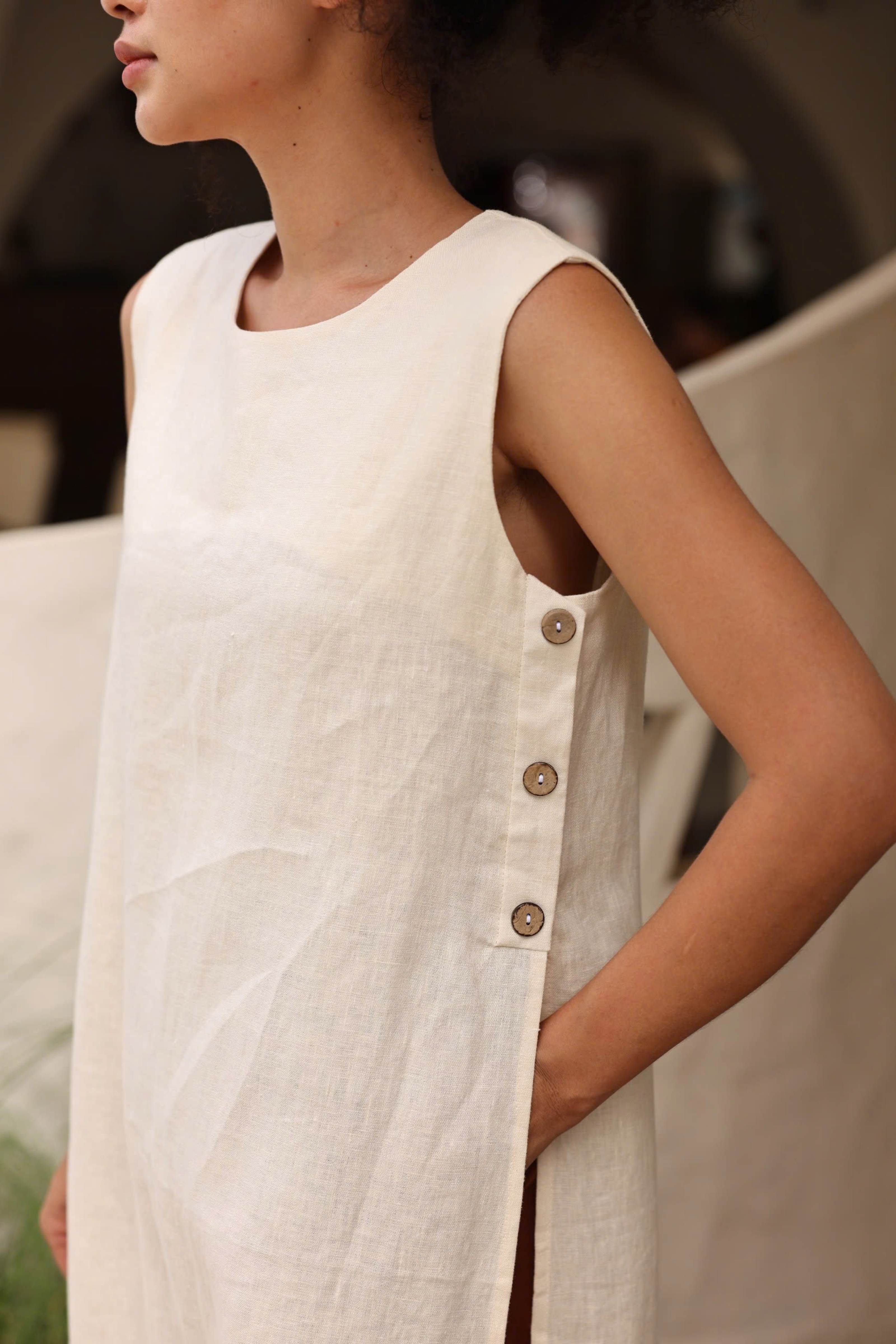 White sleeveless dress with buttons on a blurred background