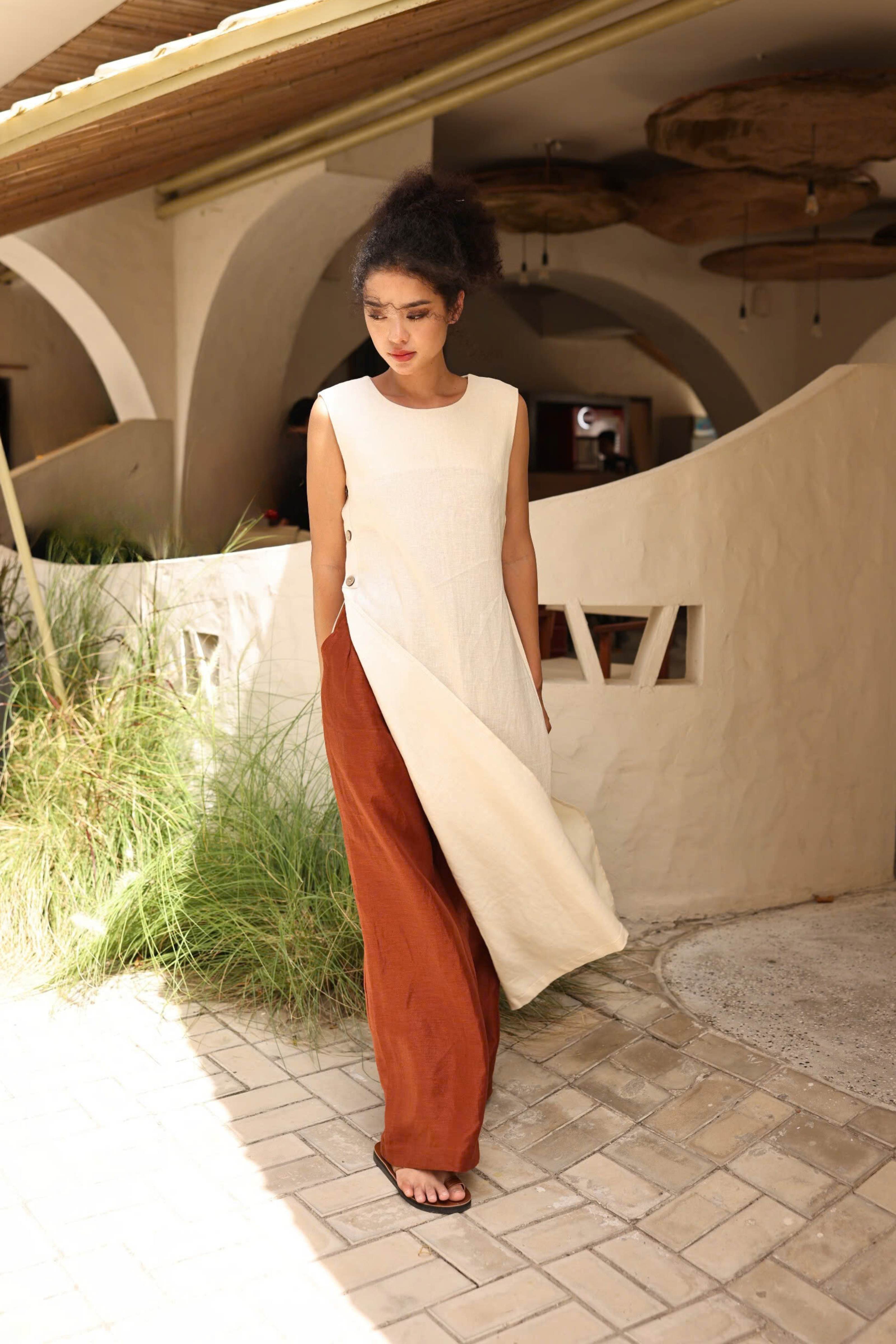 Woman in a white and rust-colored dress standing in front of a rustic building.