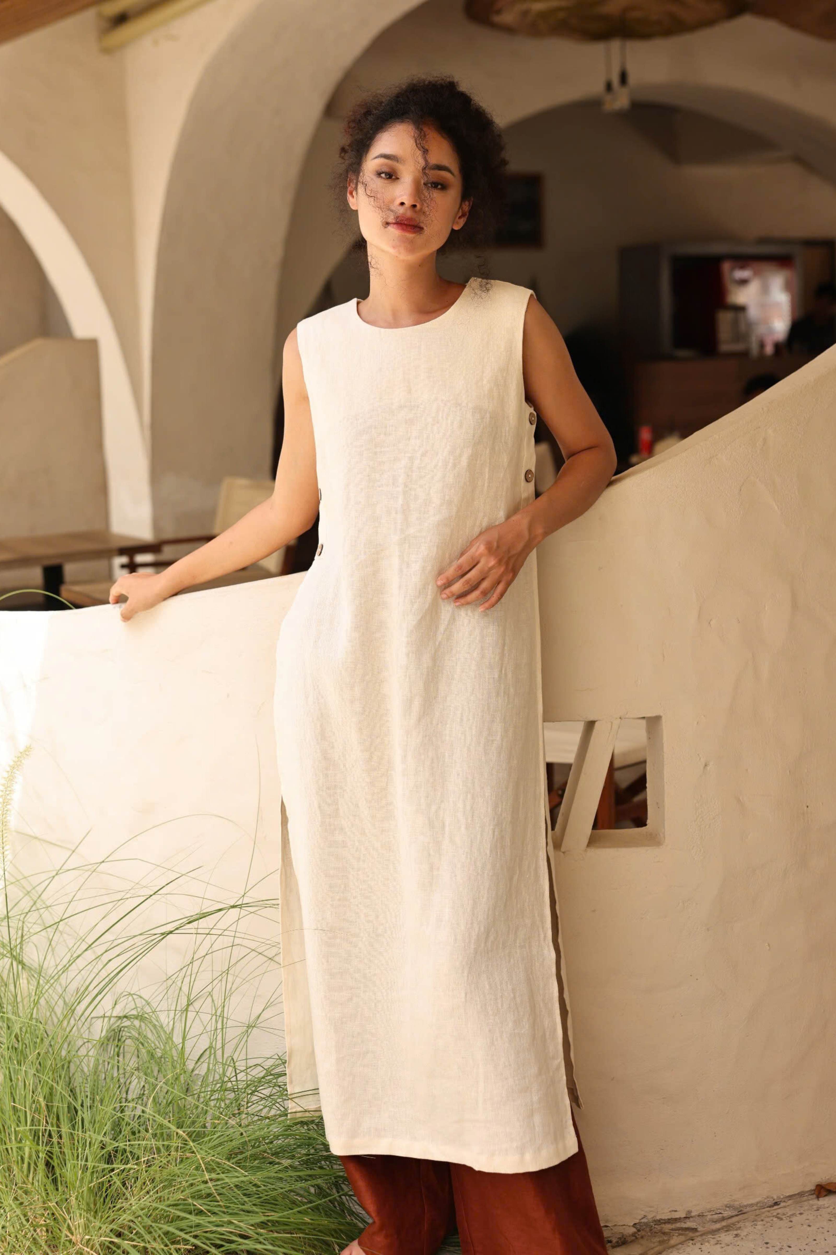 Woman wearing a long white dress standing in a sunlit room with arches.