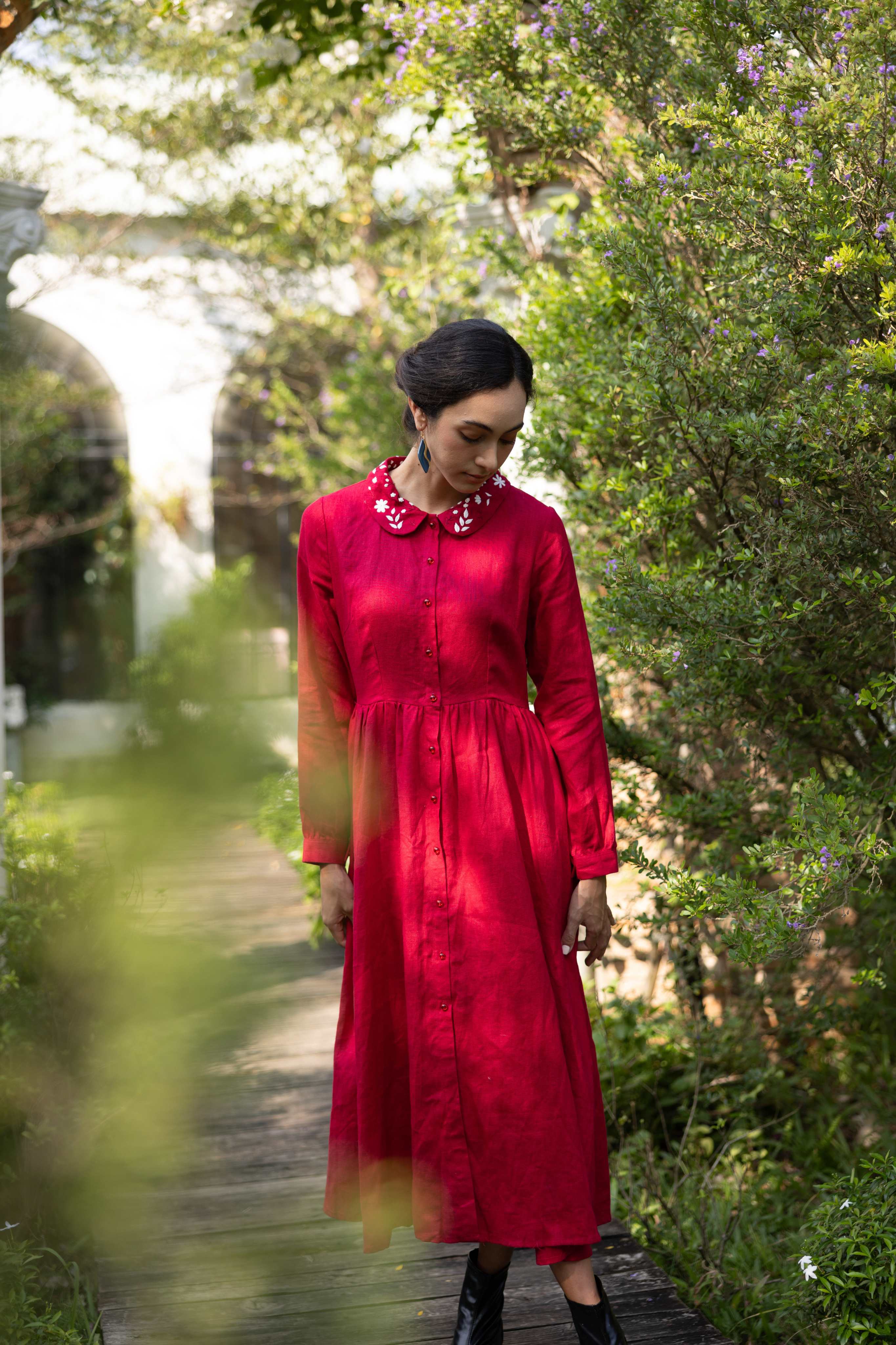 Woman in a red dress standing in a natural setting with greenery and a blurred background