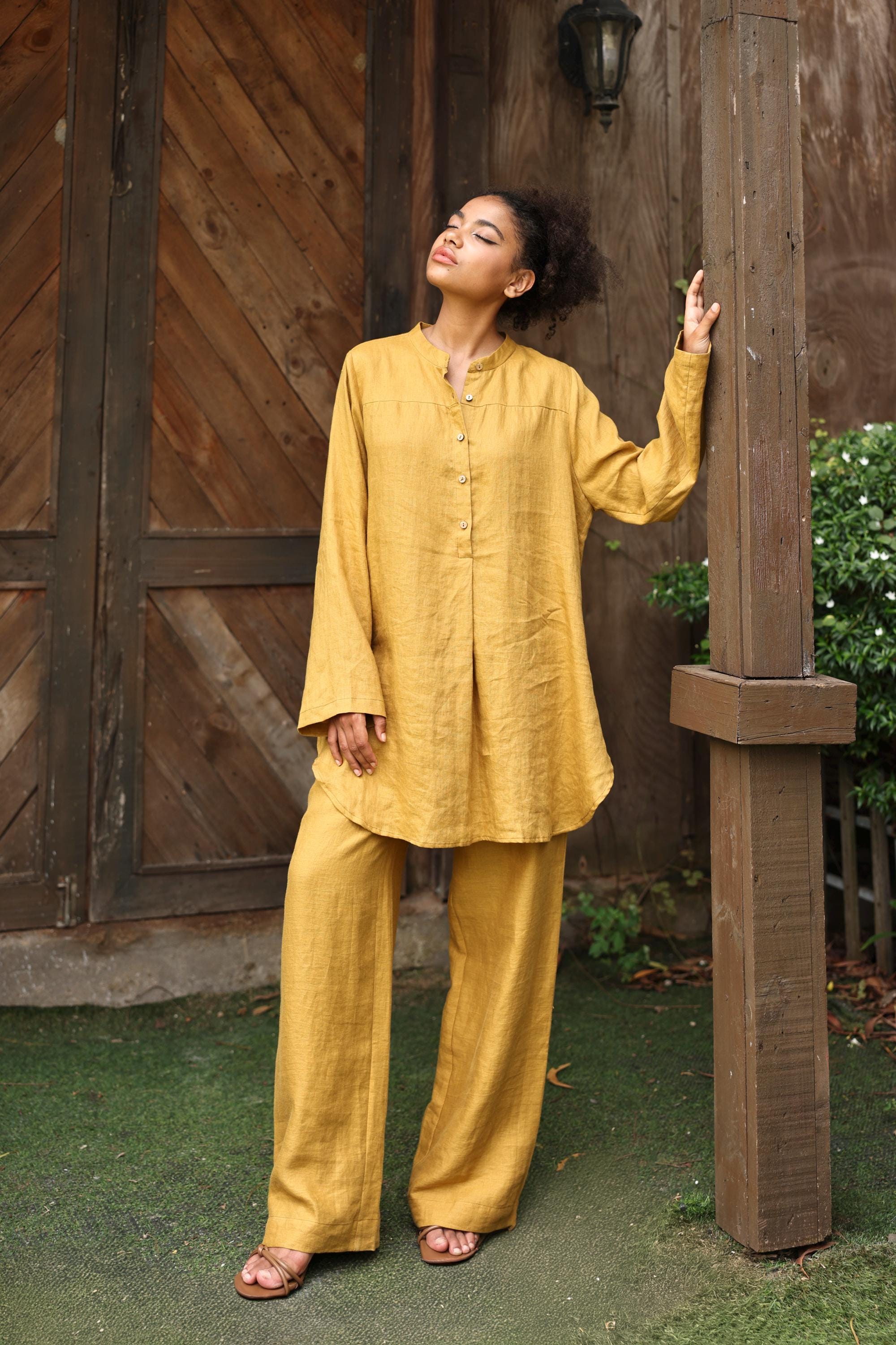 Woman in a yellow outfit standing against a wooden wall.