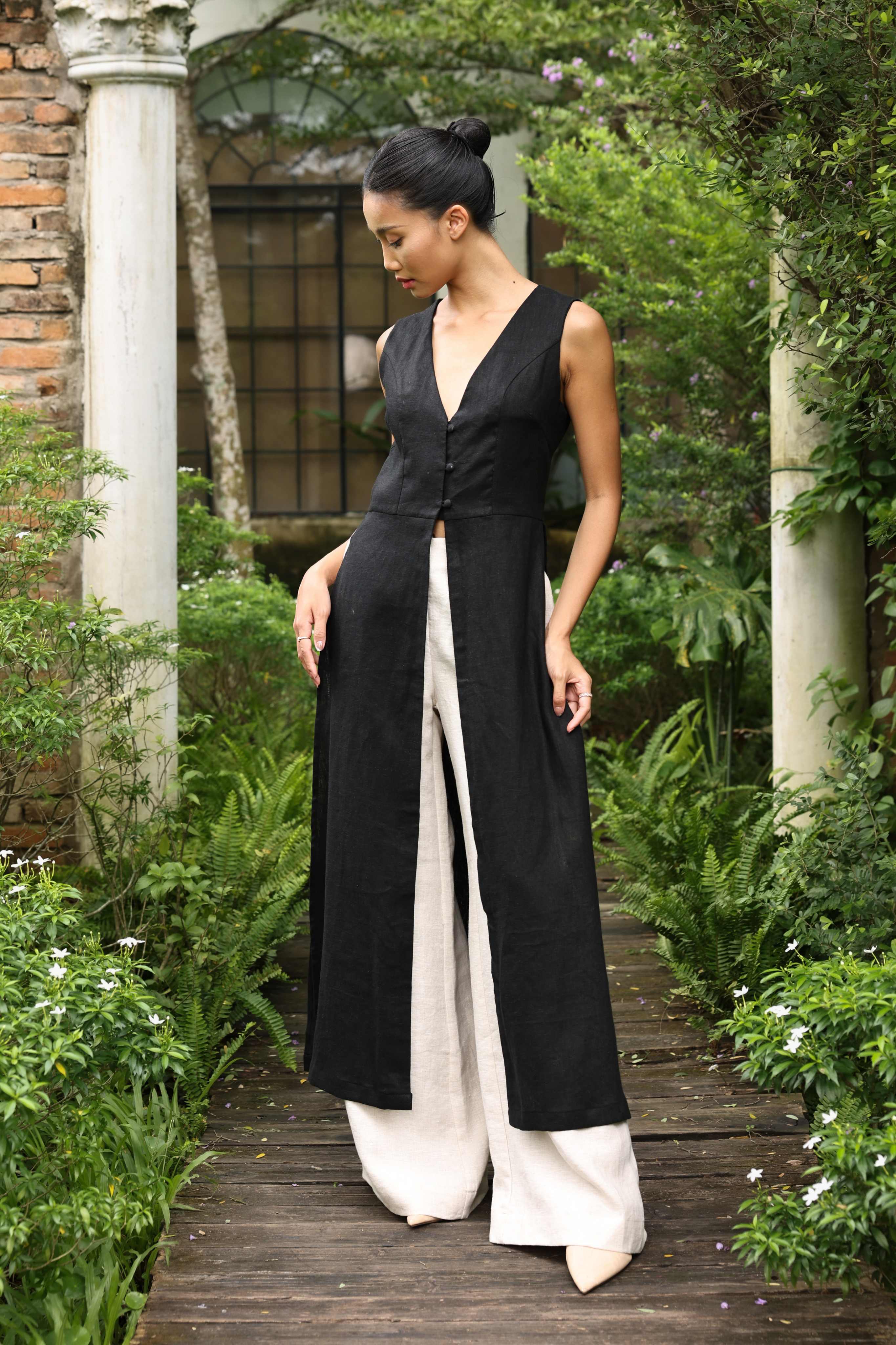 Woman wearing a long black tunic and white pants in a garden setting