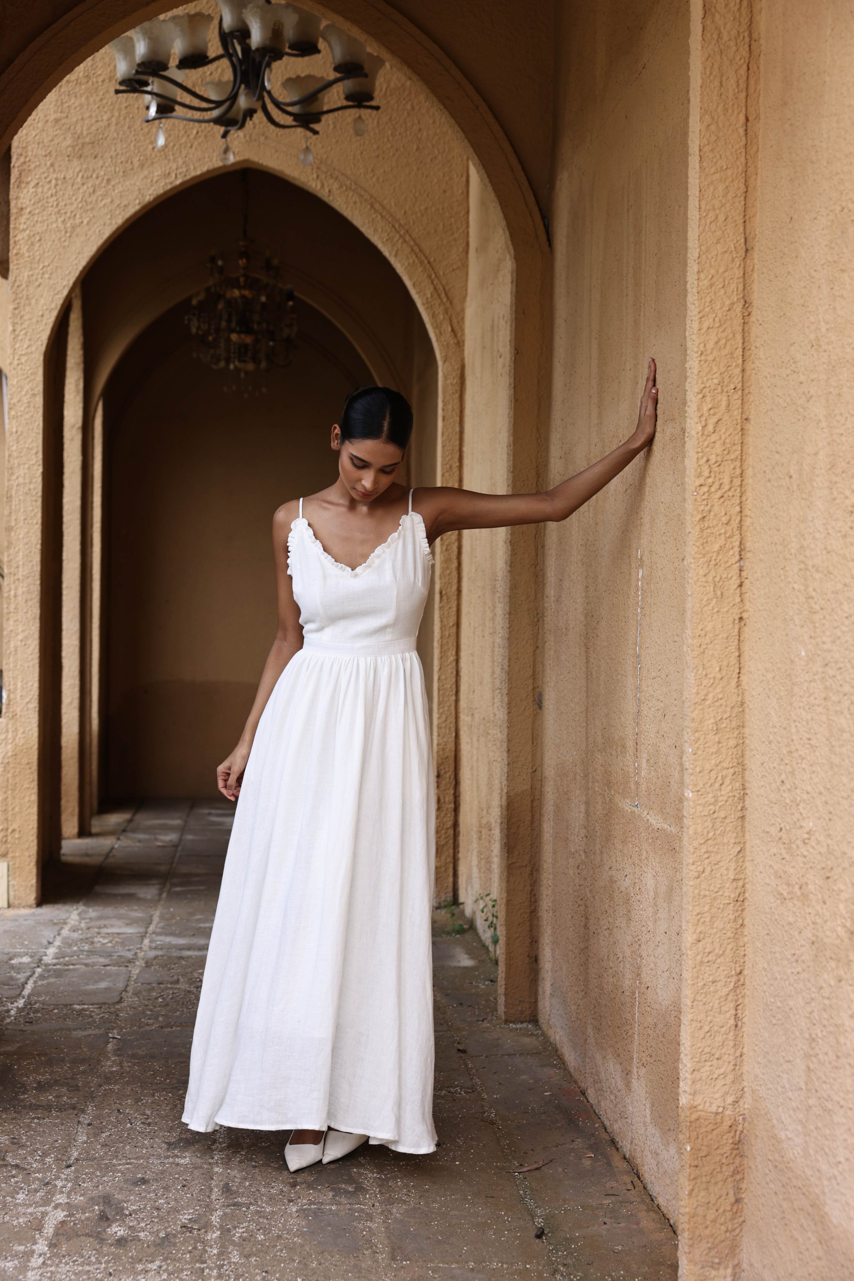 Woman in a white dress standing in an arched hallway with beige walls.