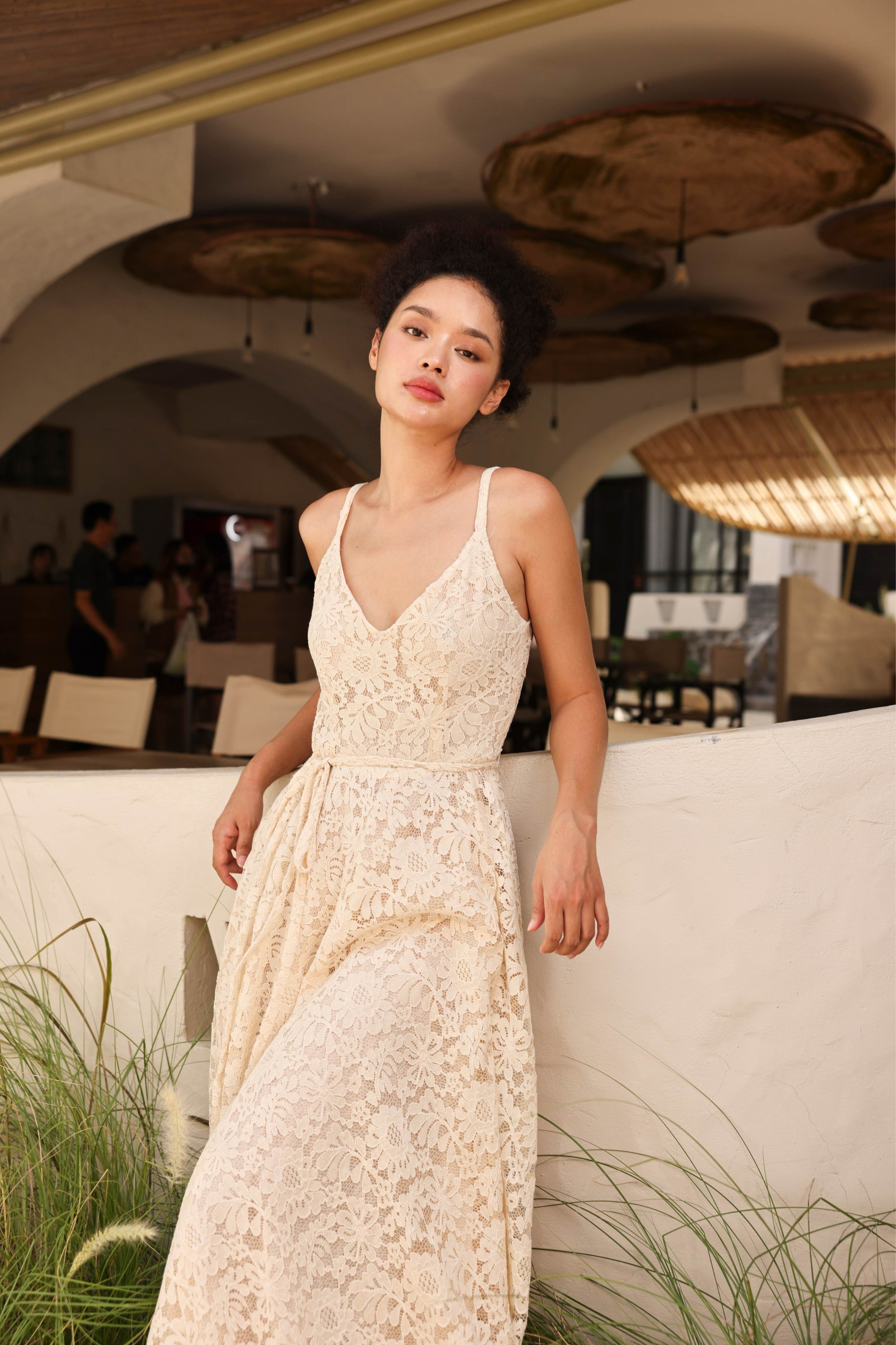 Woman in a white lace dress standing in an outdoor setting with hanging lights.