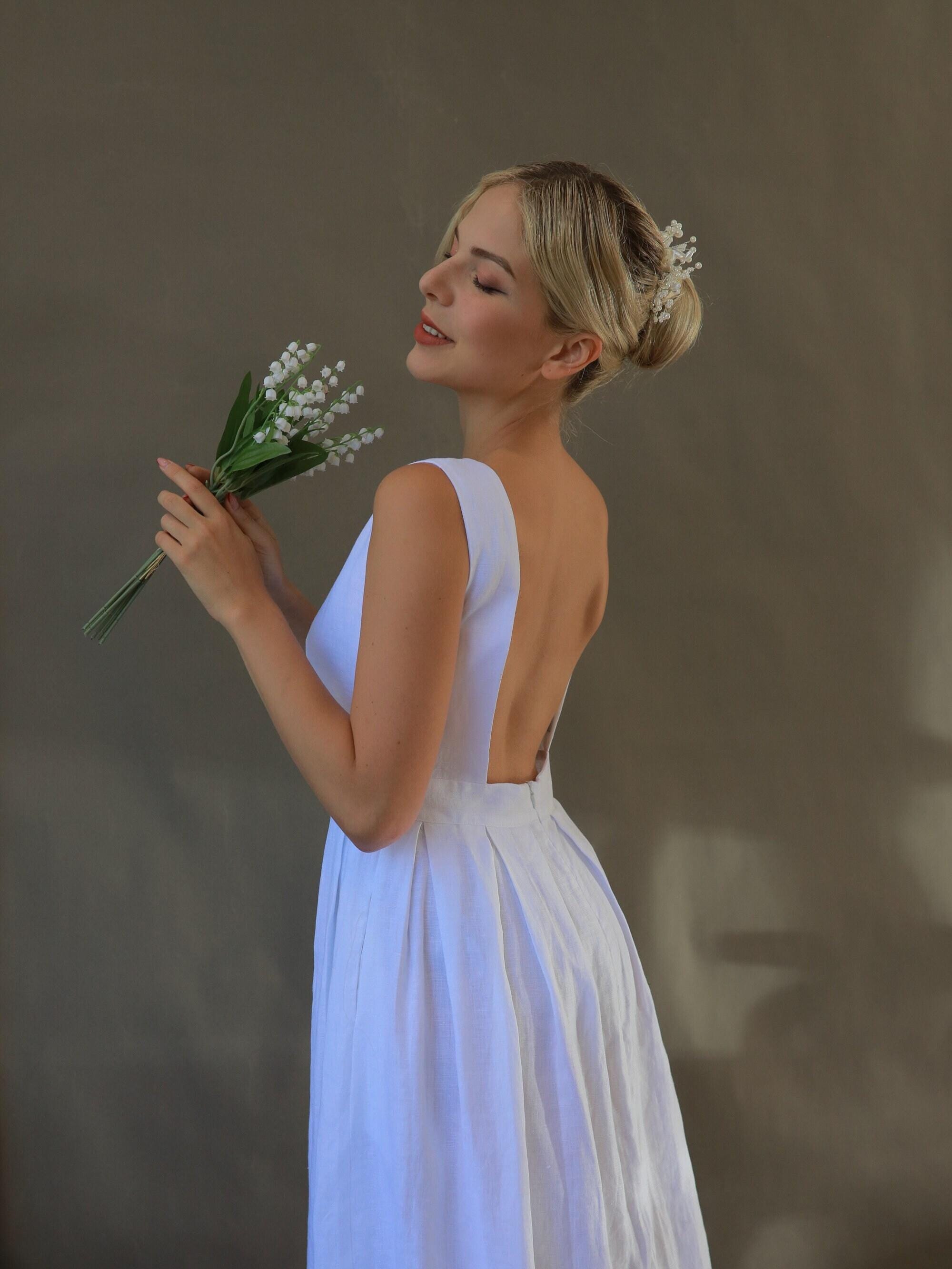 Woman in a white dress holding a bouquet against a neutral background