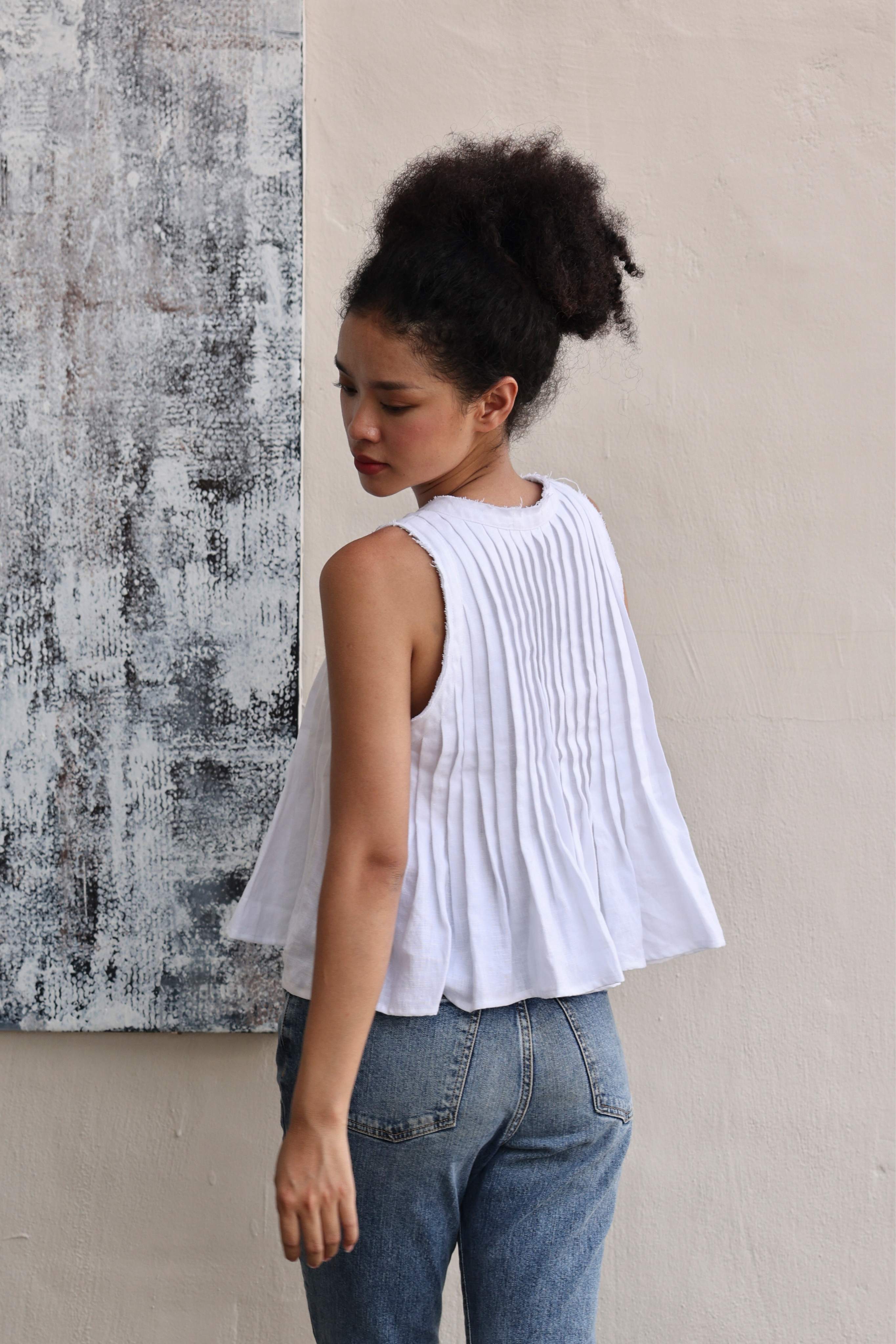 Woman wearing a white sleeveless top and blue jeans against a textured wall.