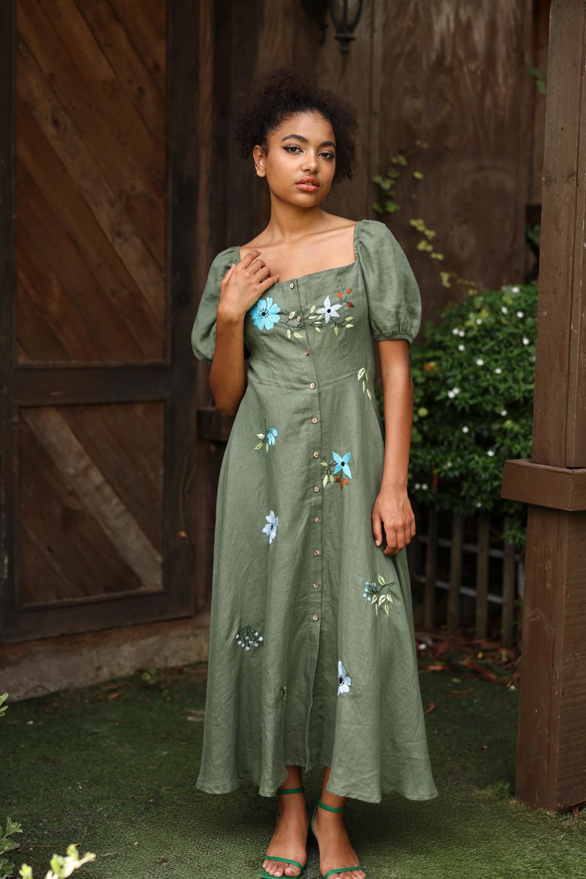 Woman wearing a green dress with floral embroidery standing outdoors.
