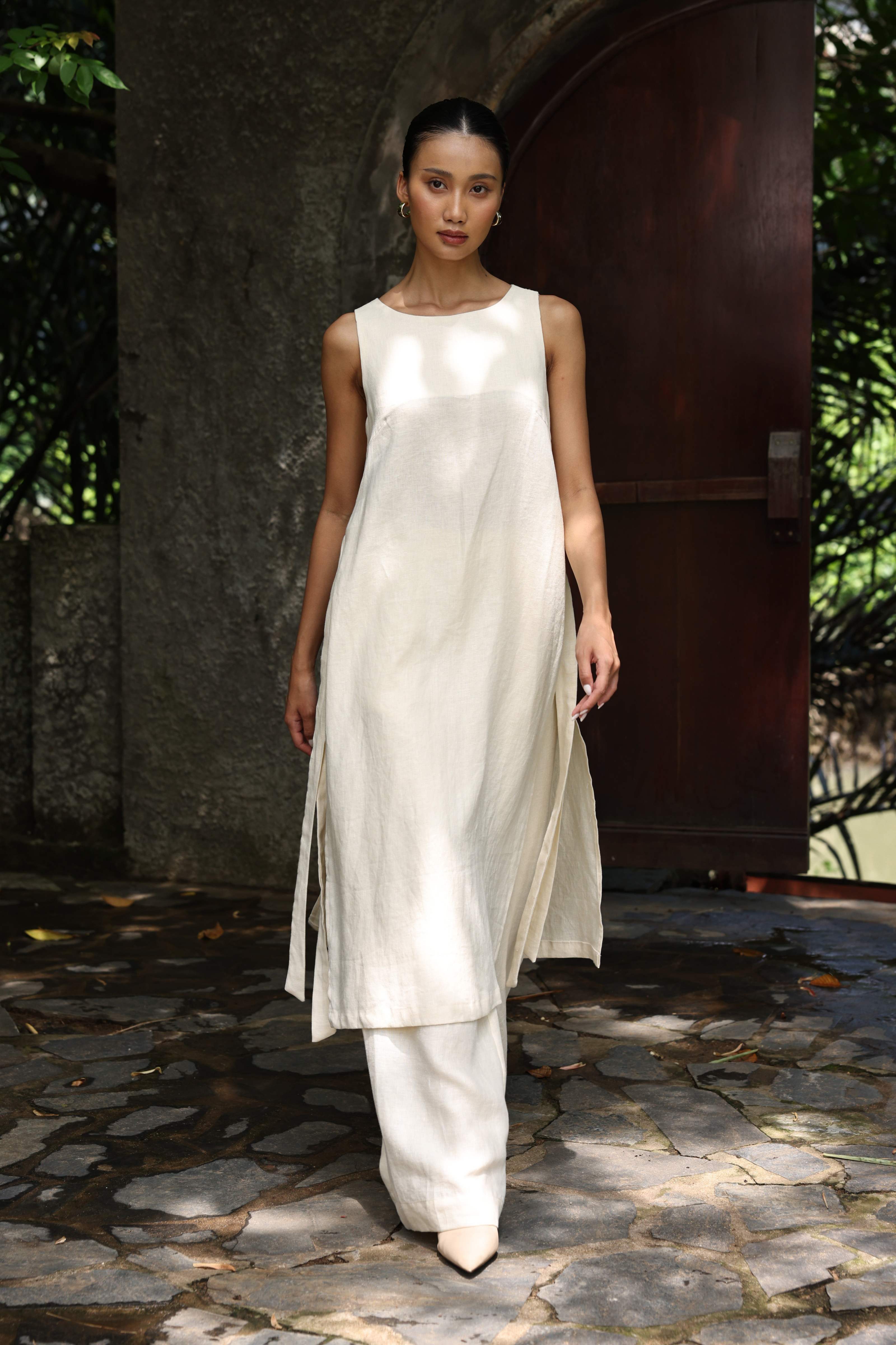 Woman wearing a white dress standing on a stone path with greenery in the background