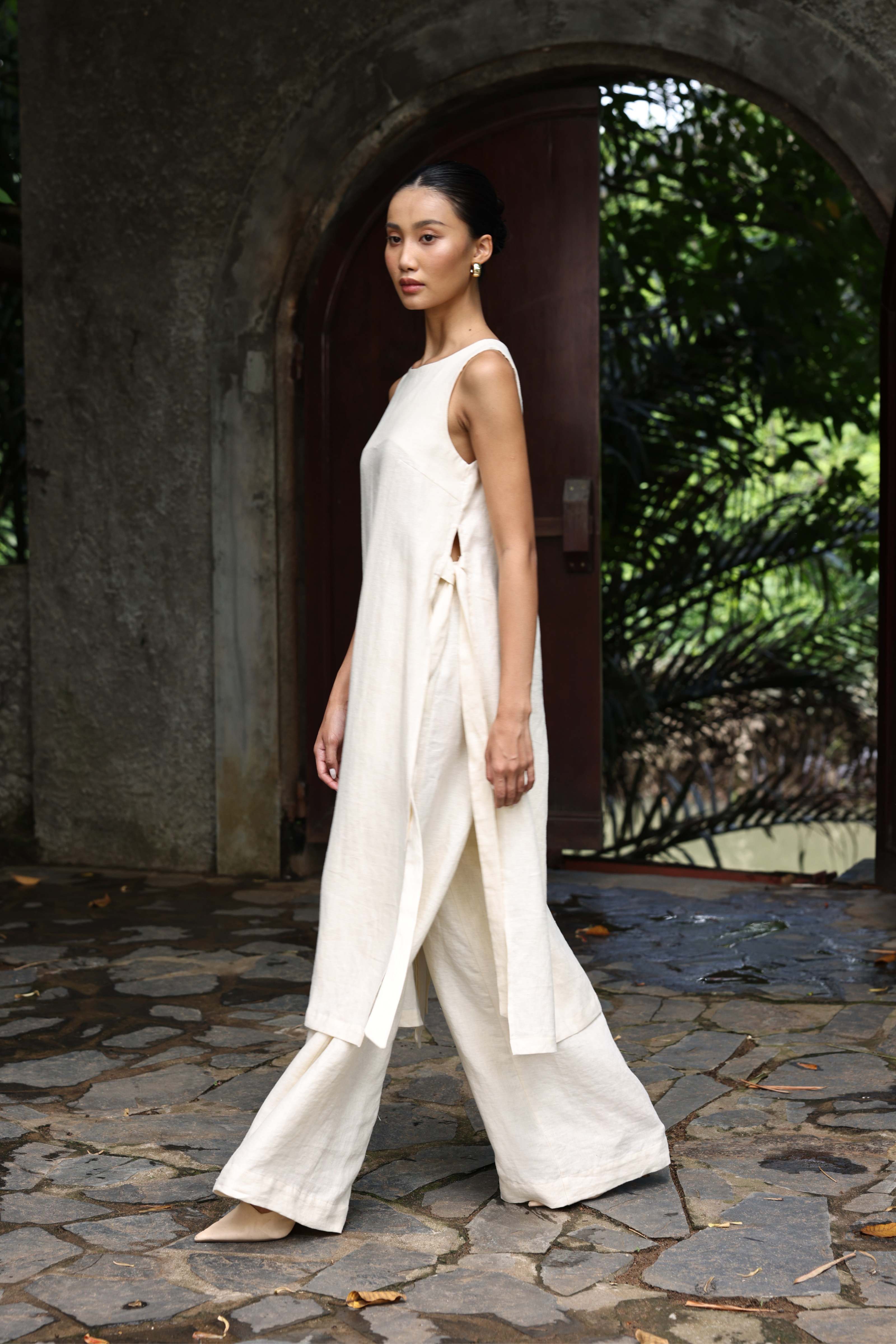 Woman in a white outfit standing in front of an archway with greenery.