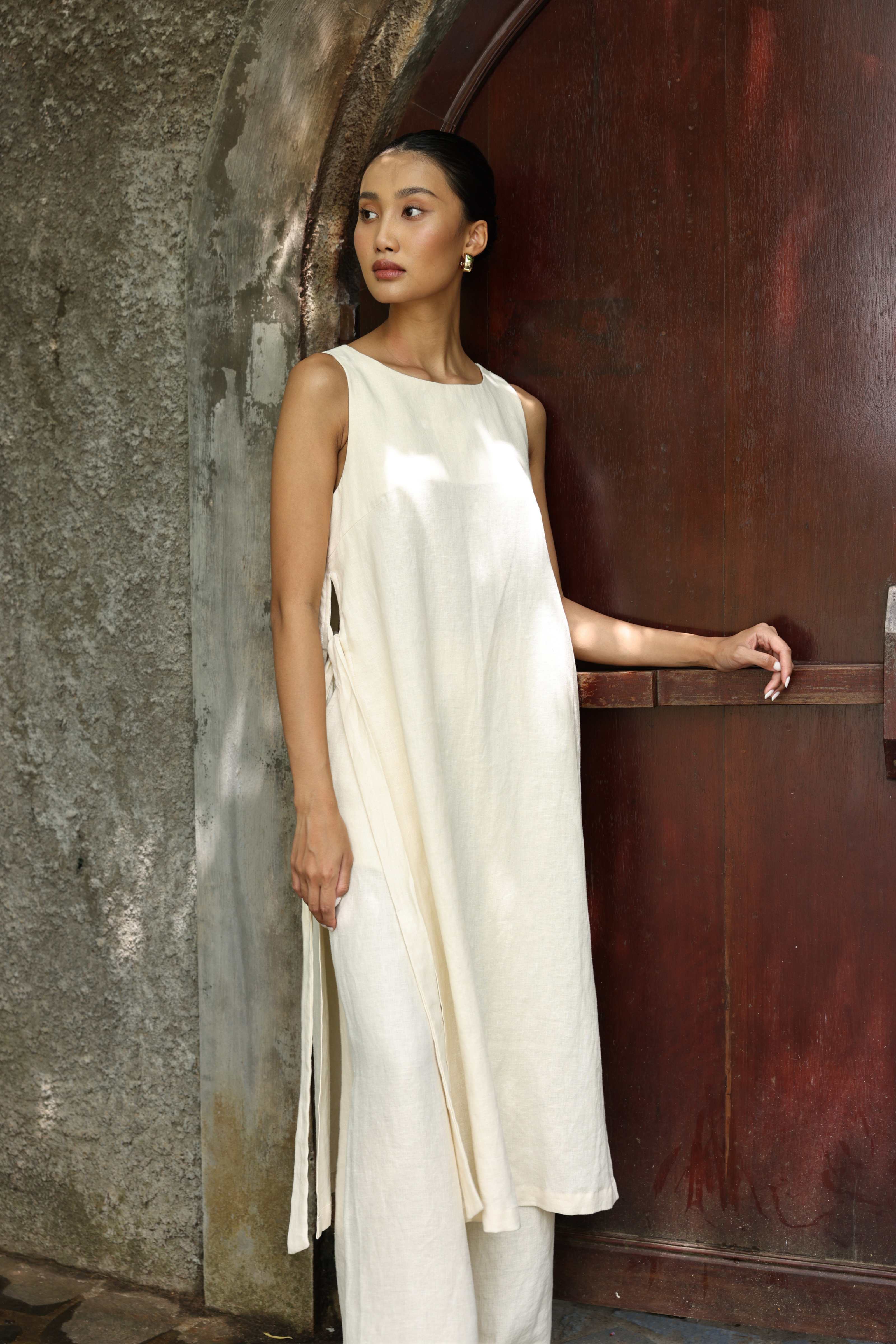 Woman in a white dress standing against a textured wall.