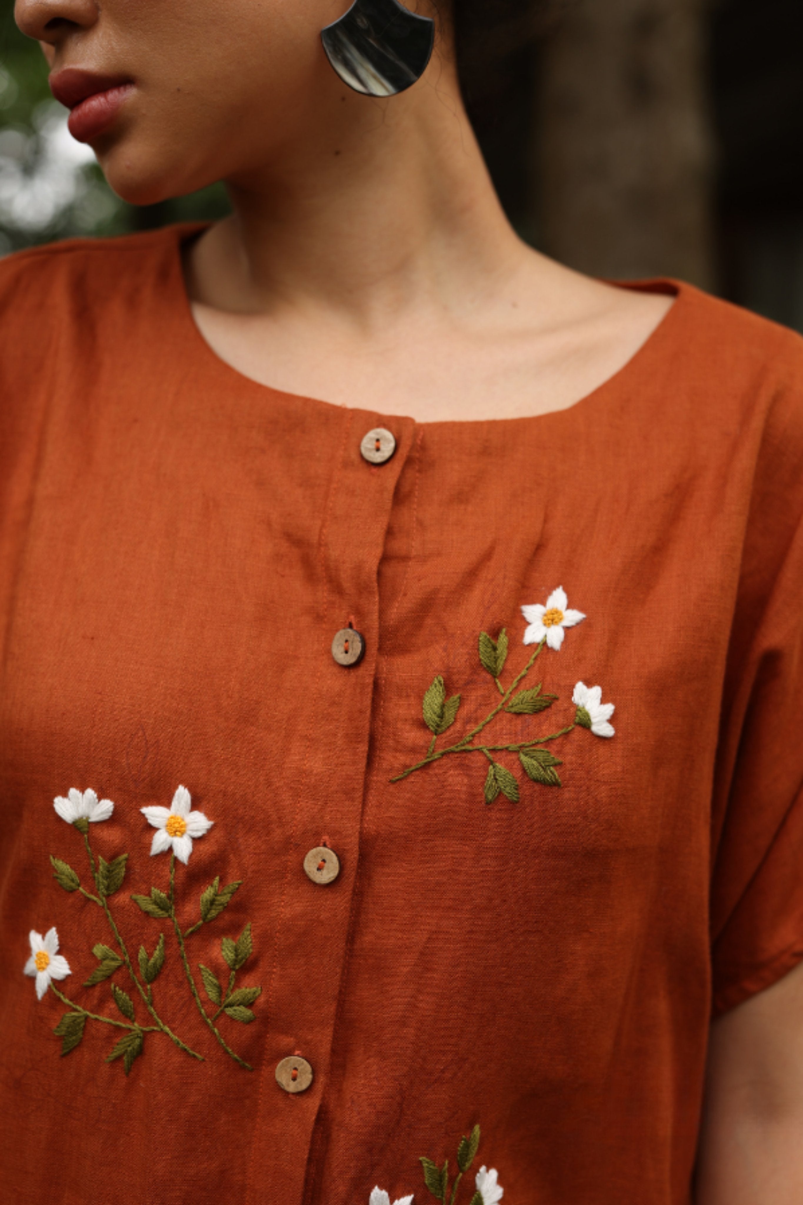 Close-up of a rust-colored dress with floral embroidery on a blurred background
