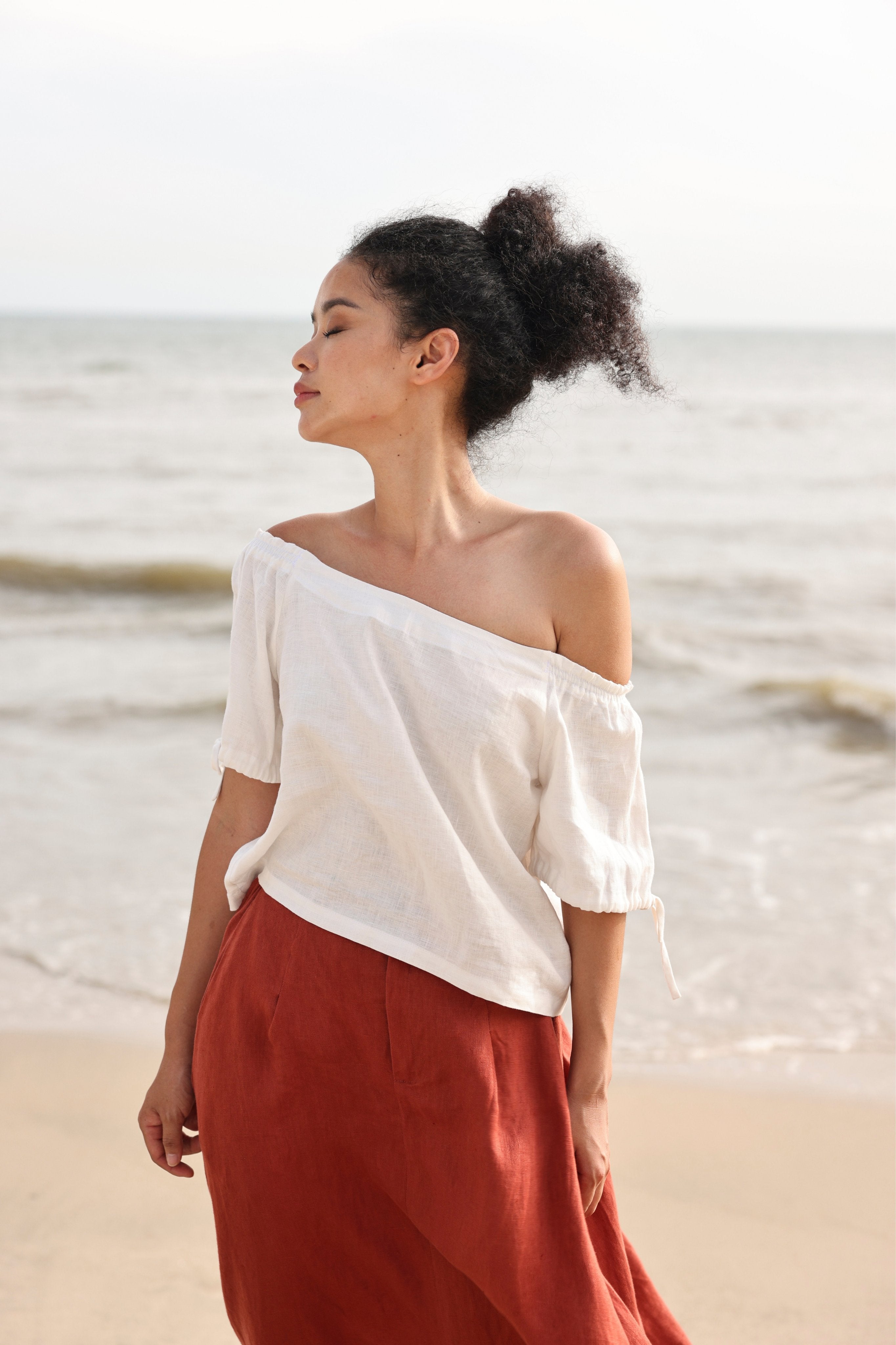 Woman in off-shoulder top and red skirt standing on a beach