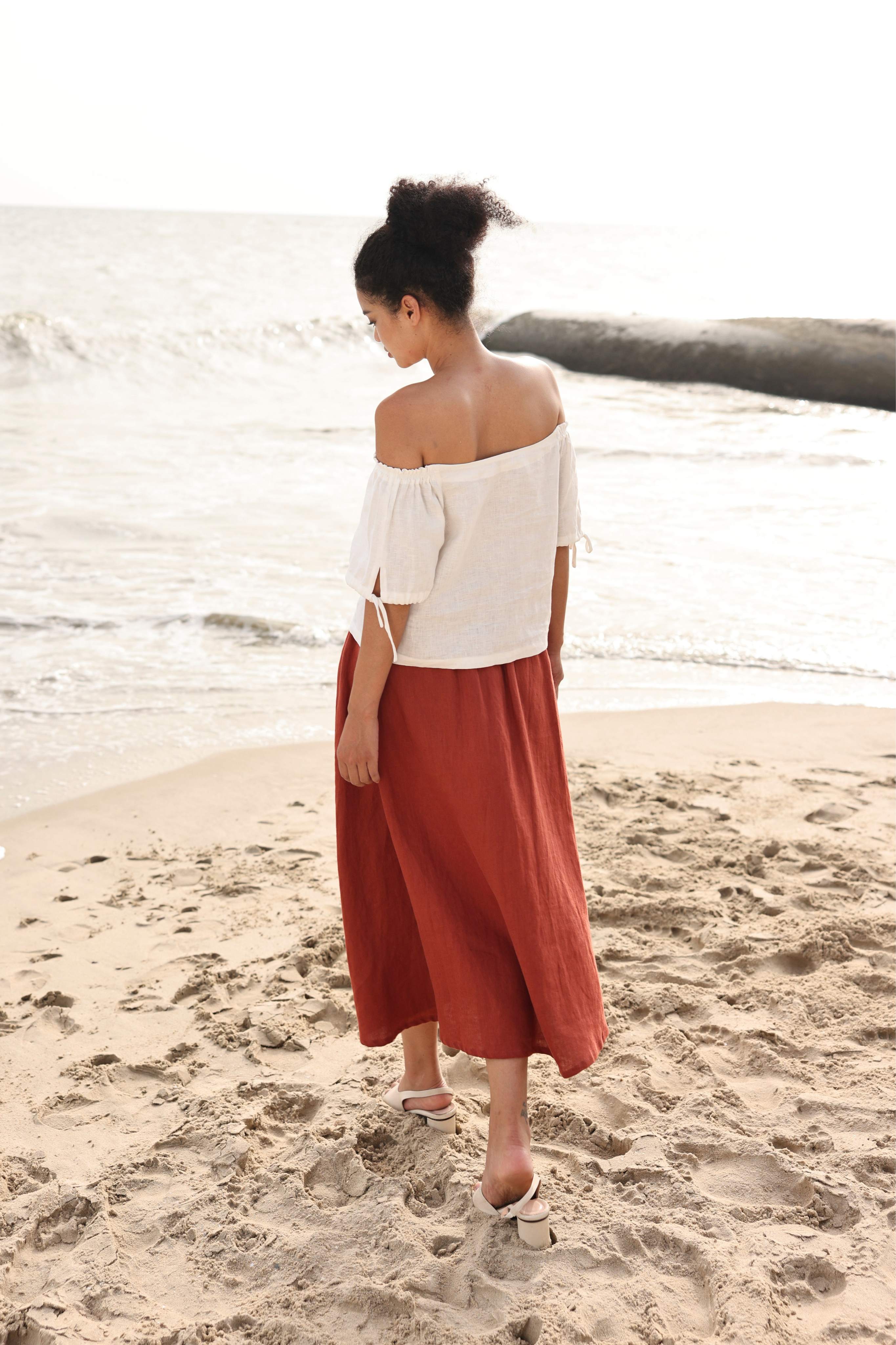 Woman in a white top and red skirt standing on a beach.