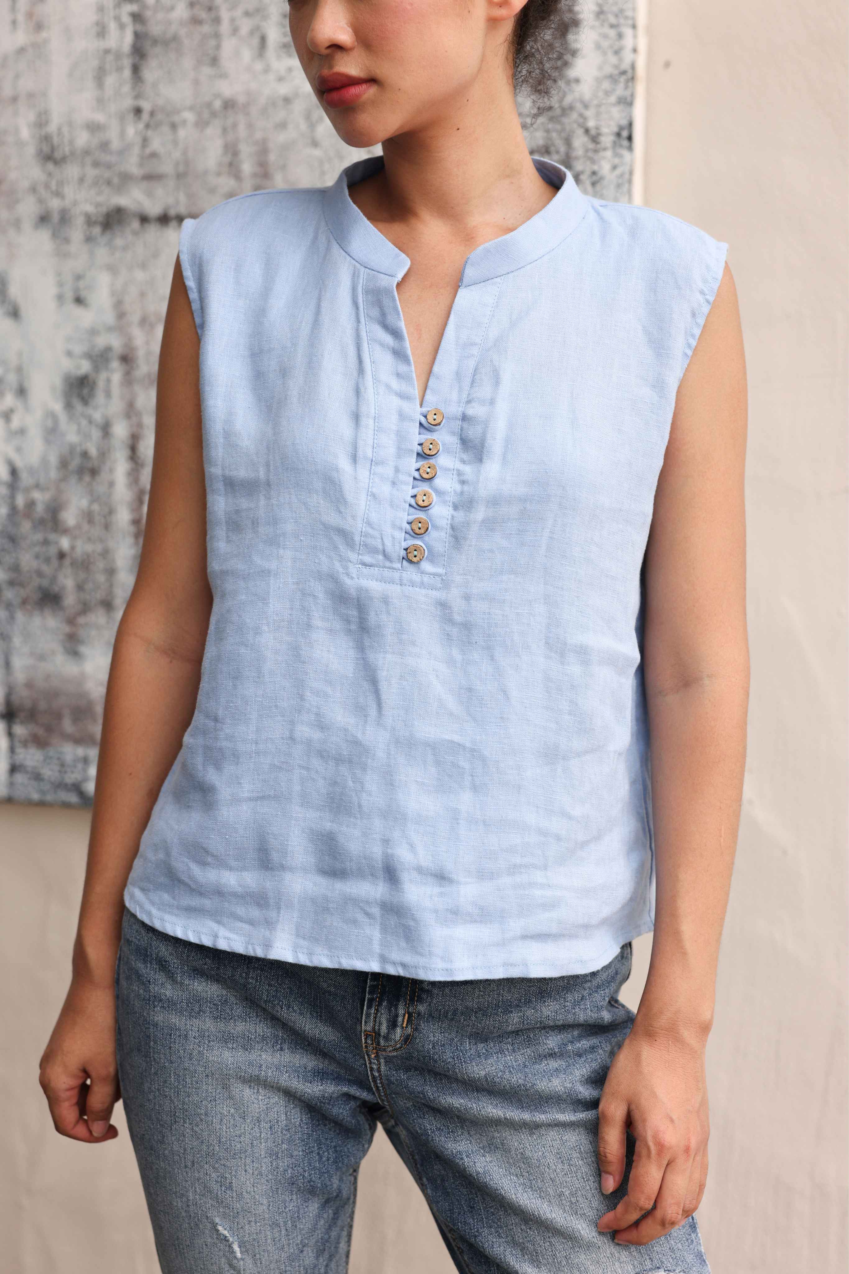 Woman wearing a light blue sleeveless top with buttons against a neutral background