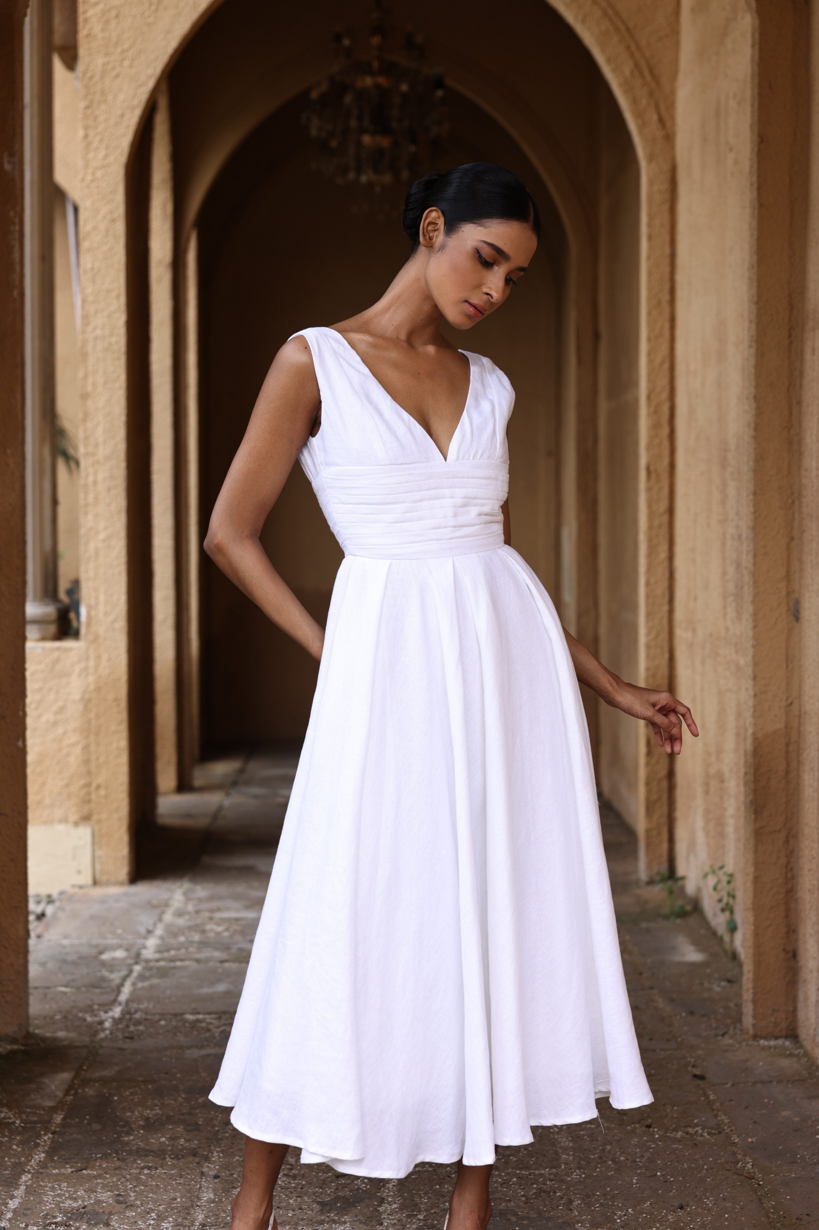 Woman in a white dress standing in an arched stone corridor