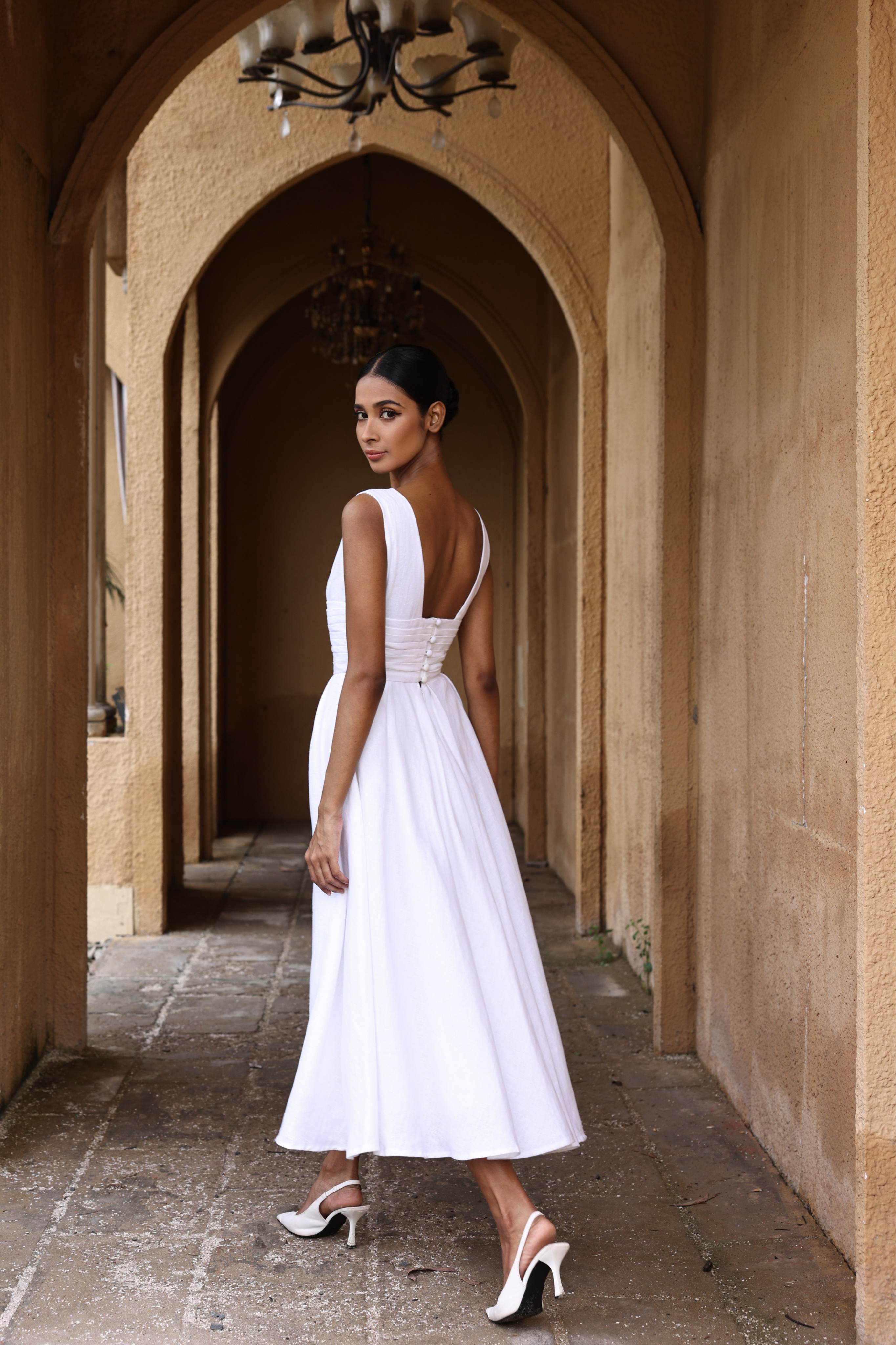 Woman in a white dress standing in an arched hallway with beige walls.