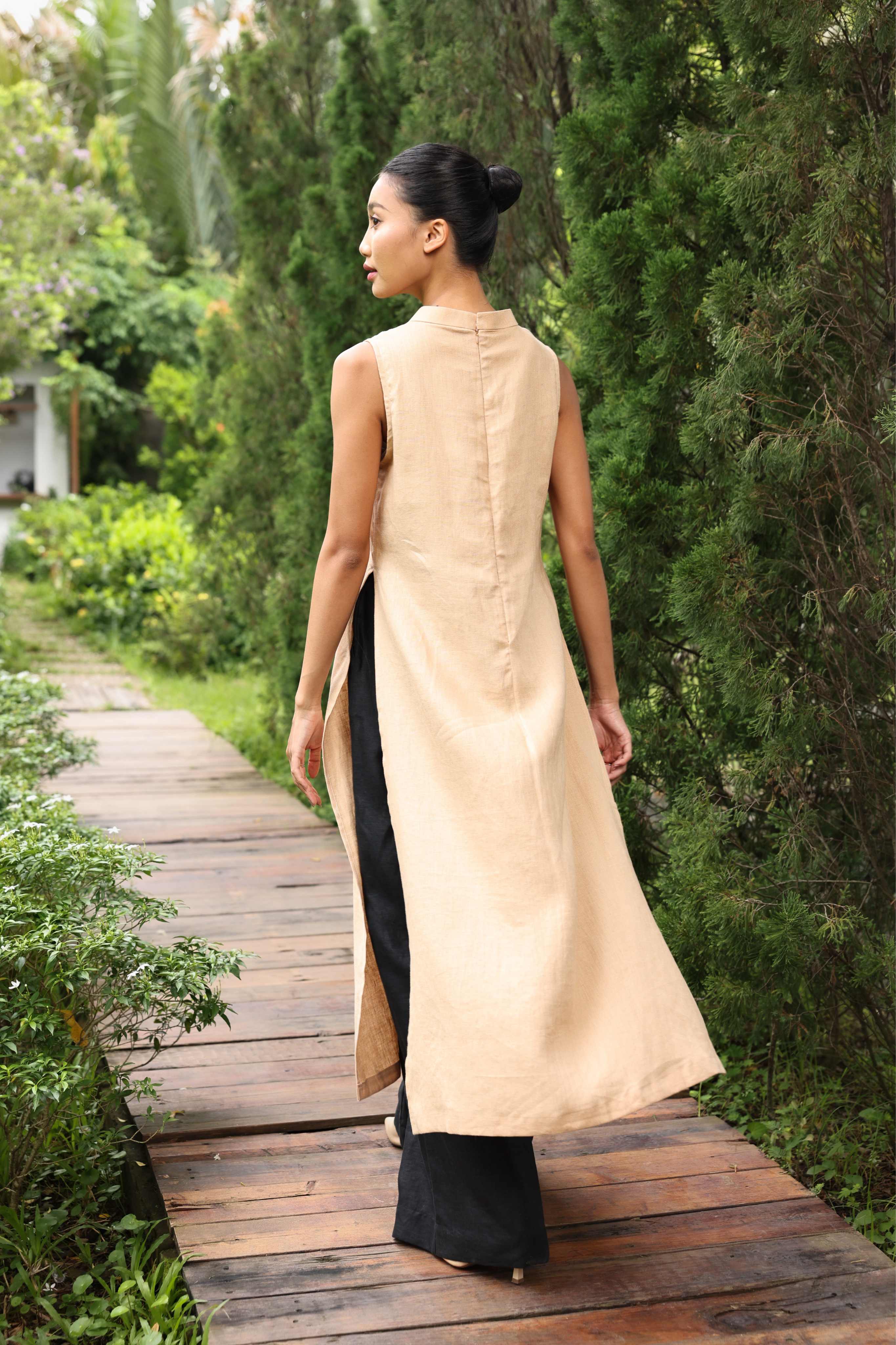 Woman in a beige kurta with black pants walking on a wooden path in a garden.