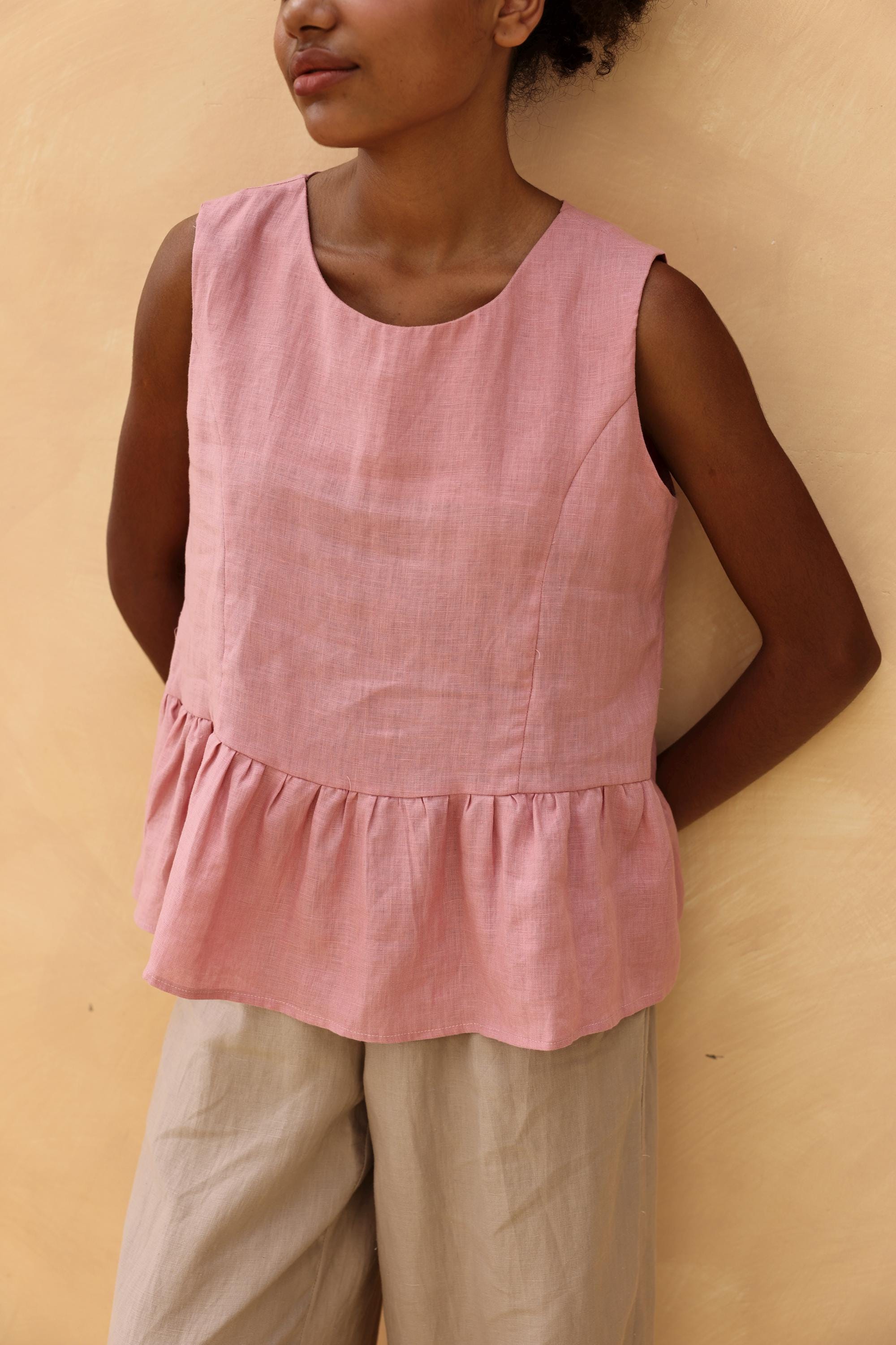 Person wearing a pink sleeveless top with a ruffled hem against a beige background
