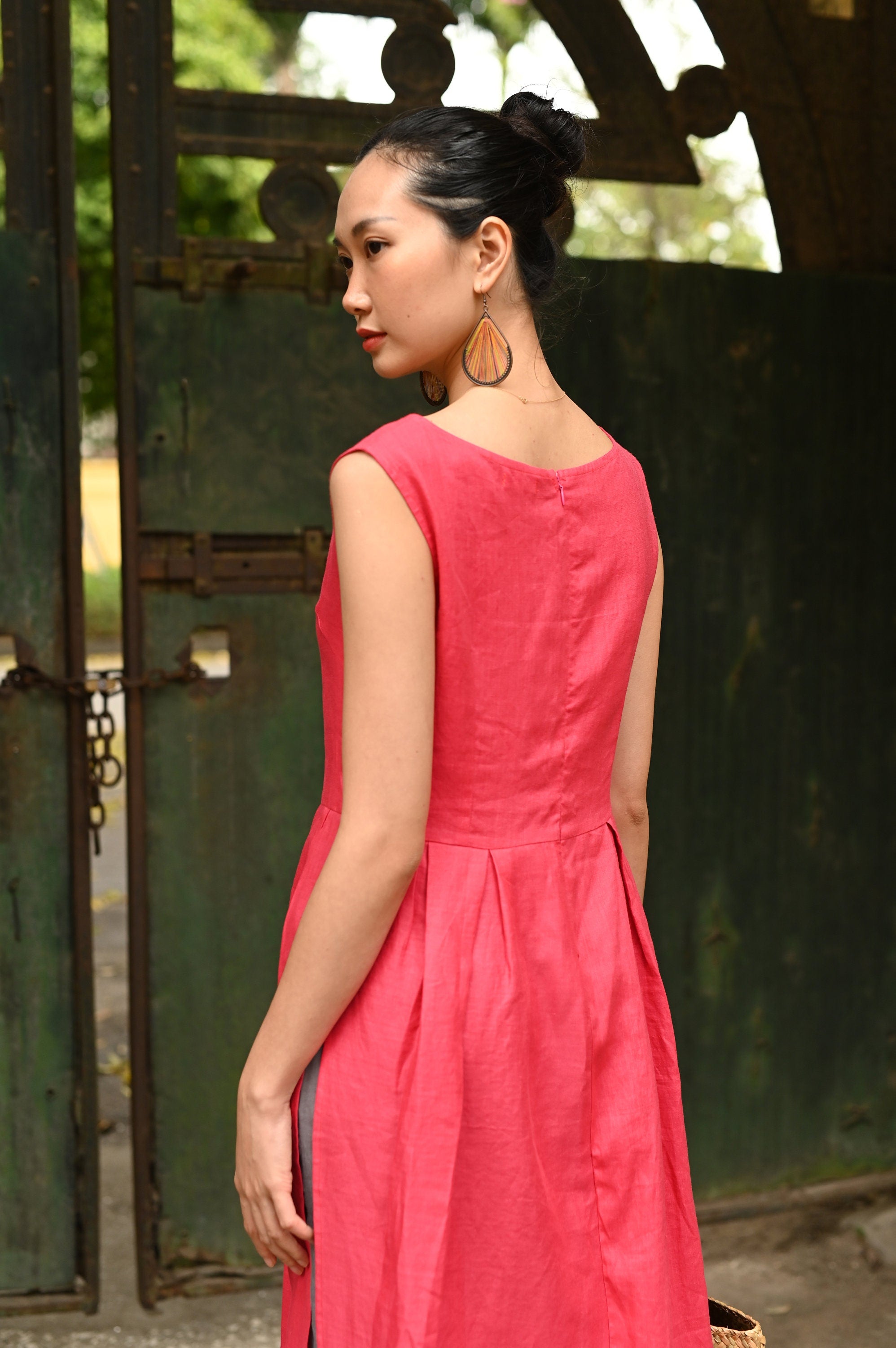 Woman in a pink dress standing in front of a green metal gate.