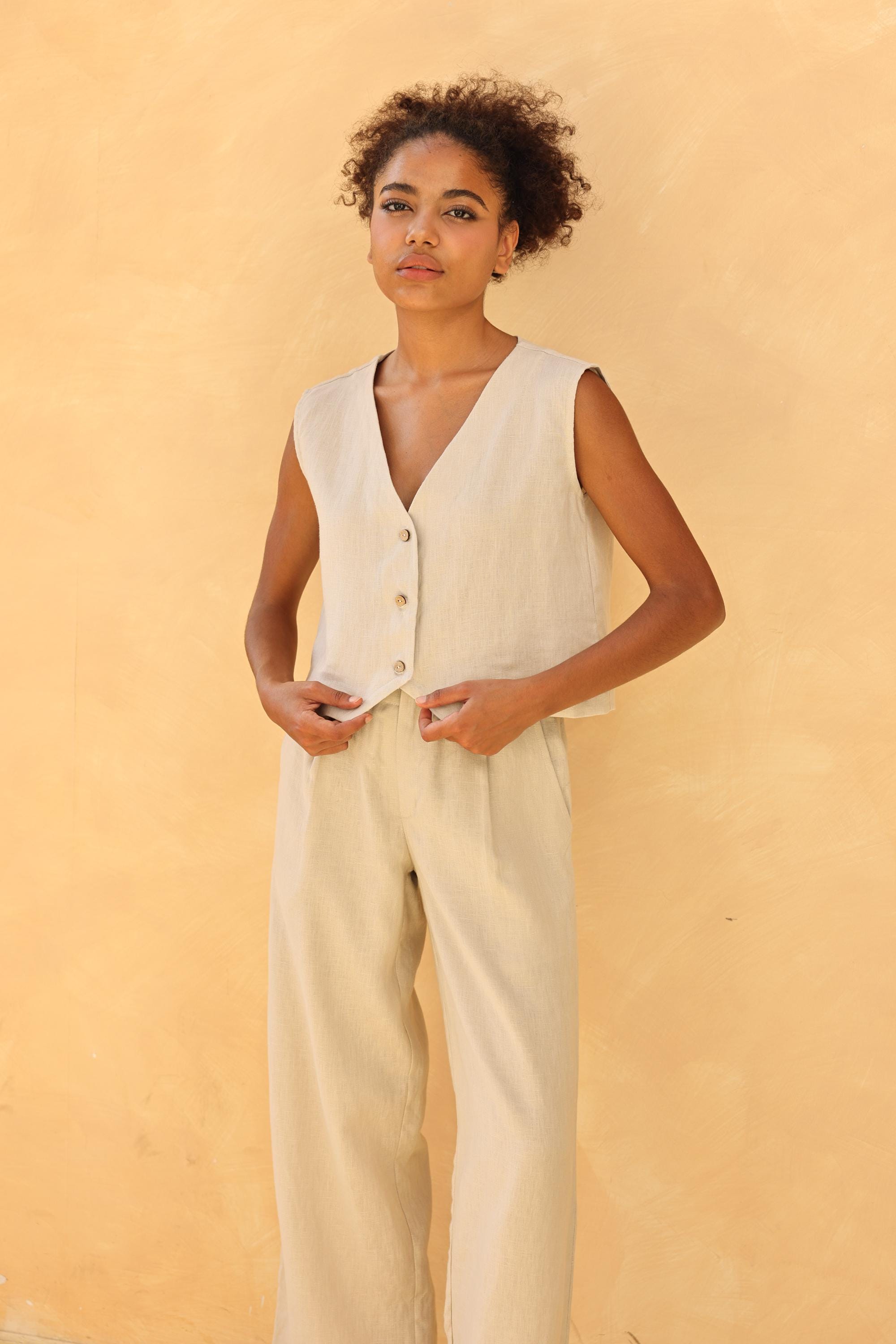 Woman wearing a beige vest and pants against a yellow background