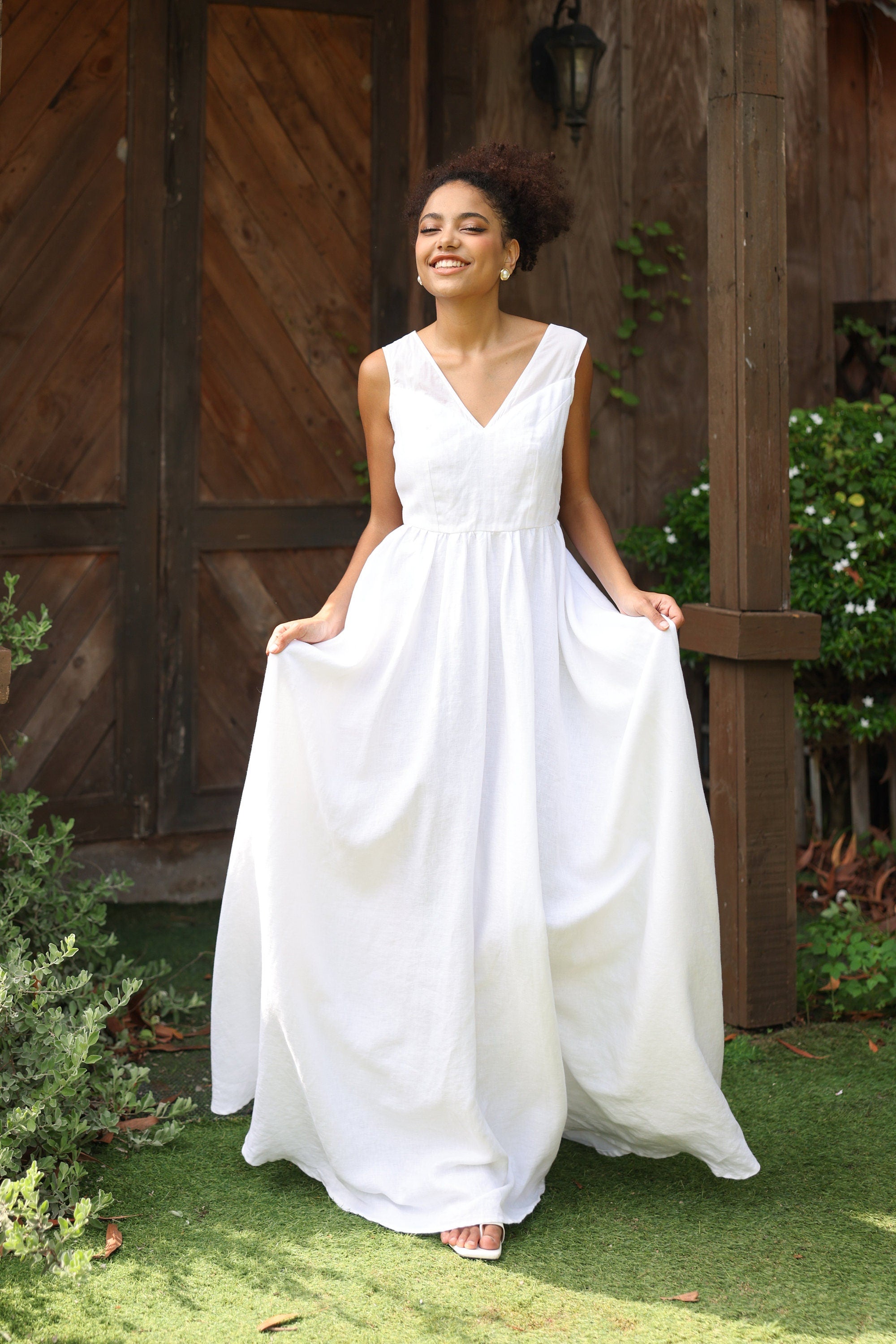 Woman in a white dress standing outdoors with wooden doors and greenery in the background