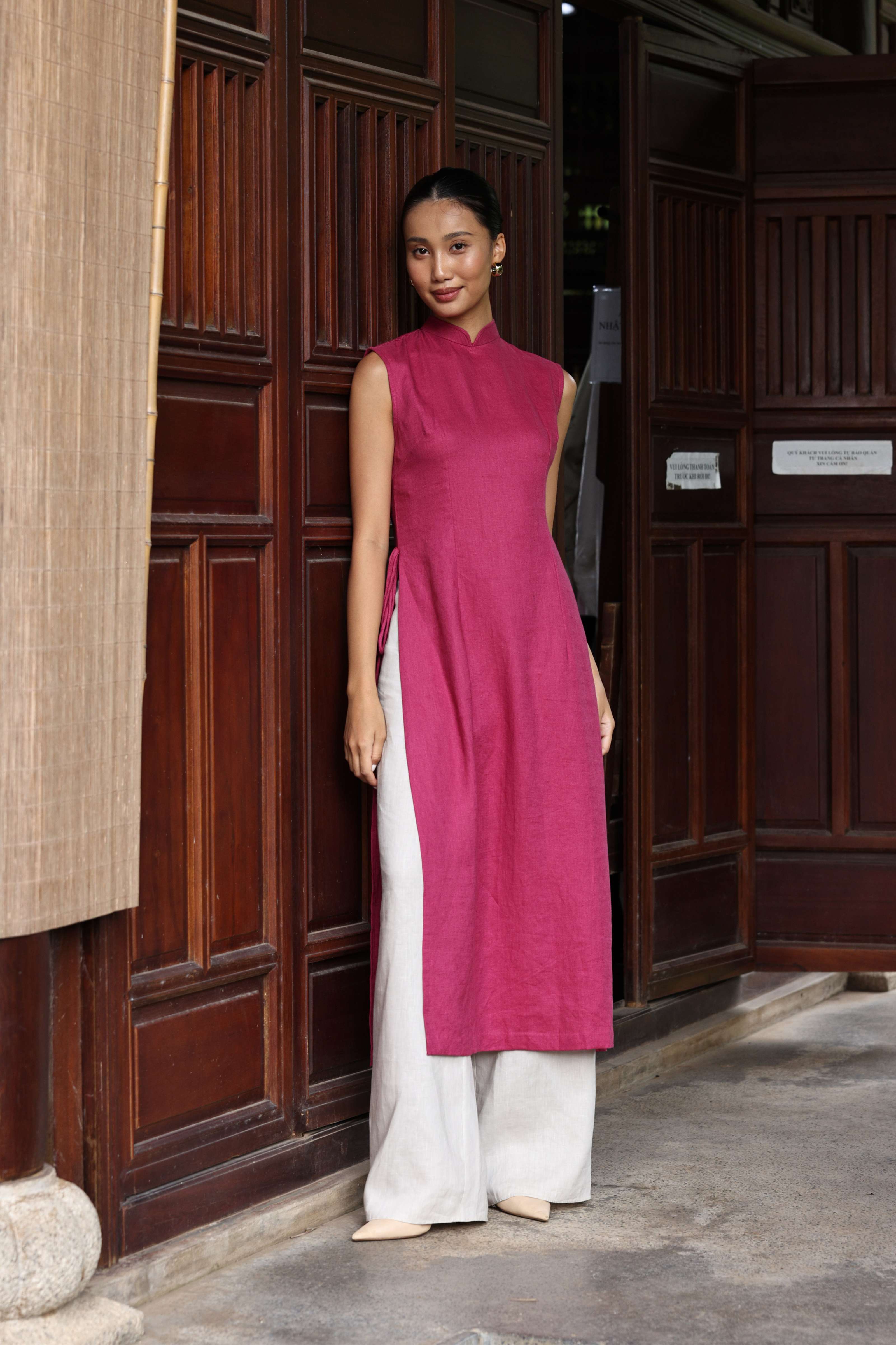 Woman wearing a pink and white dress standing in front of wooden doors.