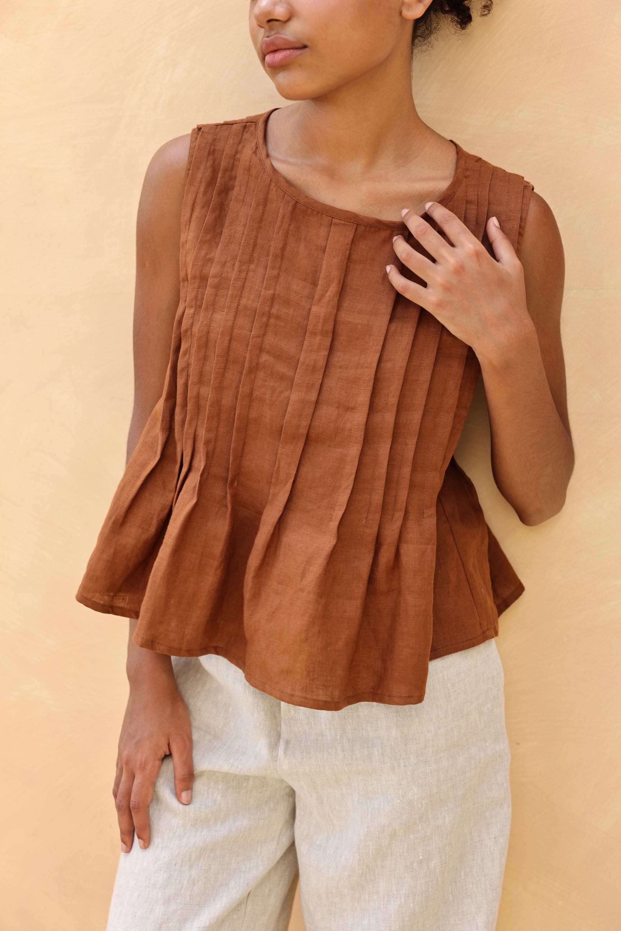 Woman wearing a brown sleeveless top against a beige background