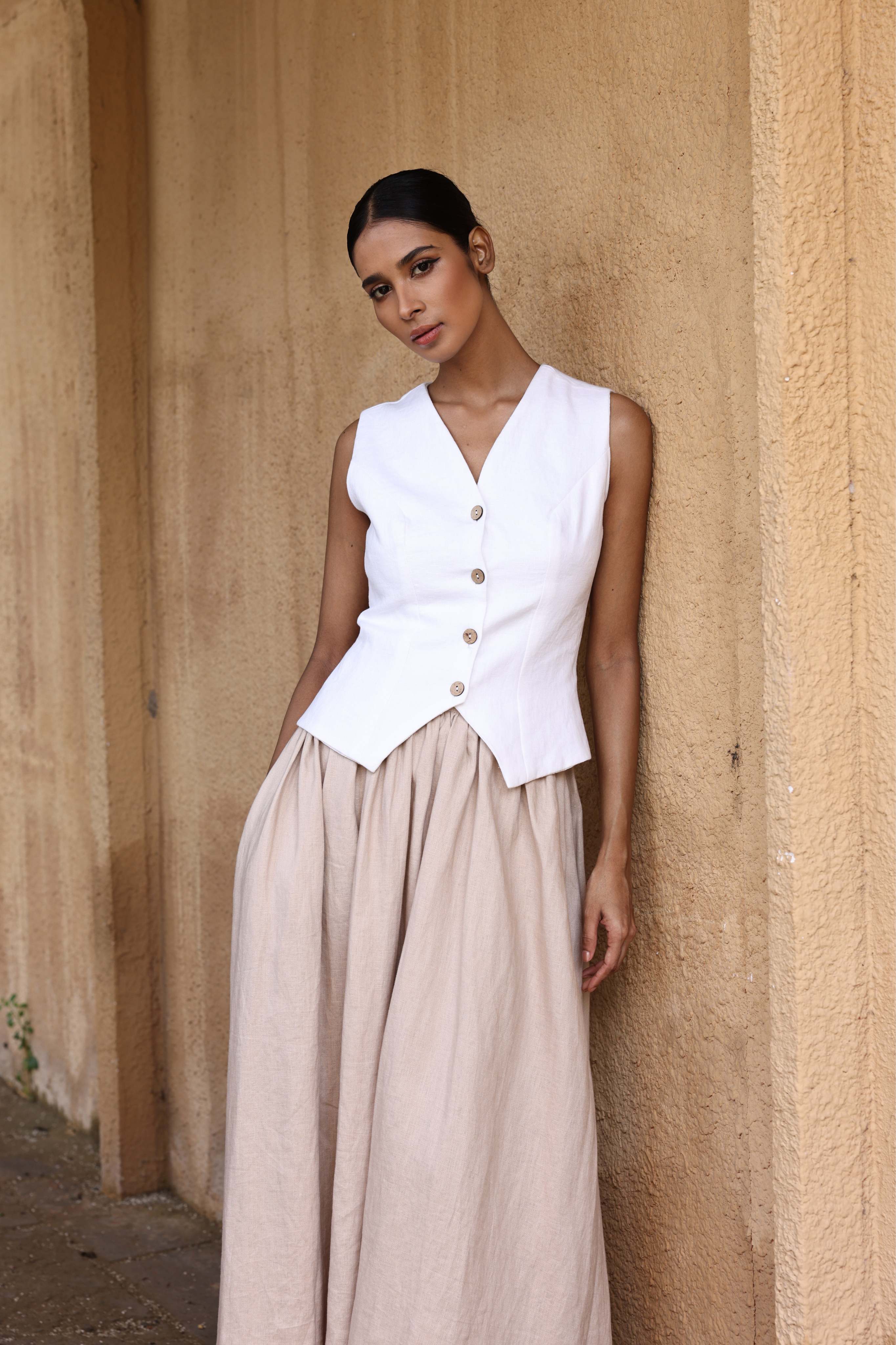Woman wearing a white sleeveless top and beige skirt against a beige wall.