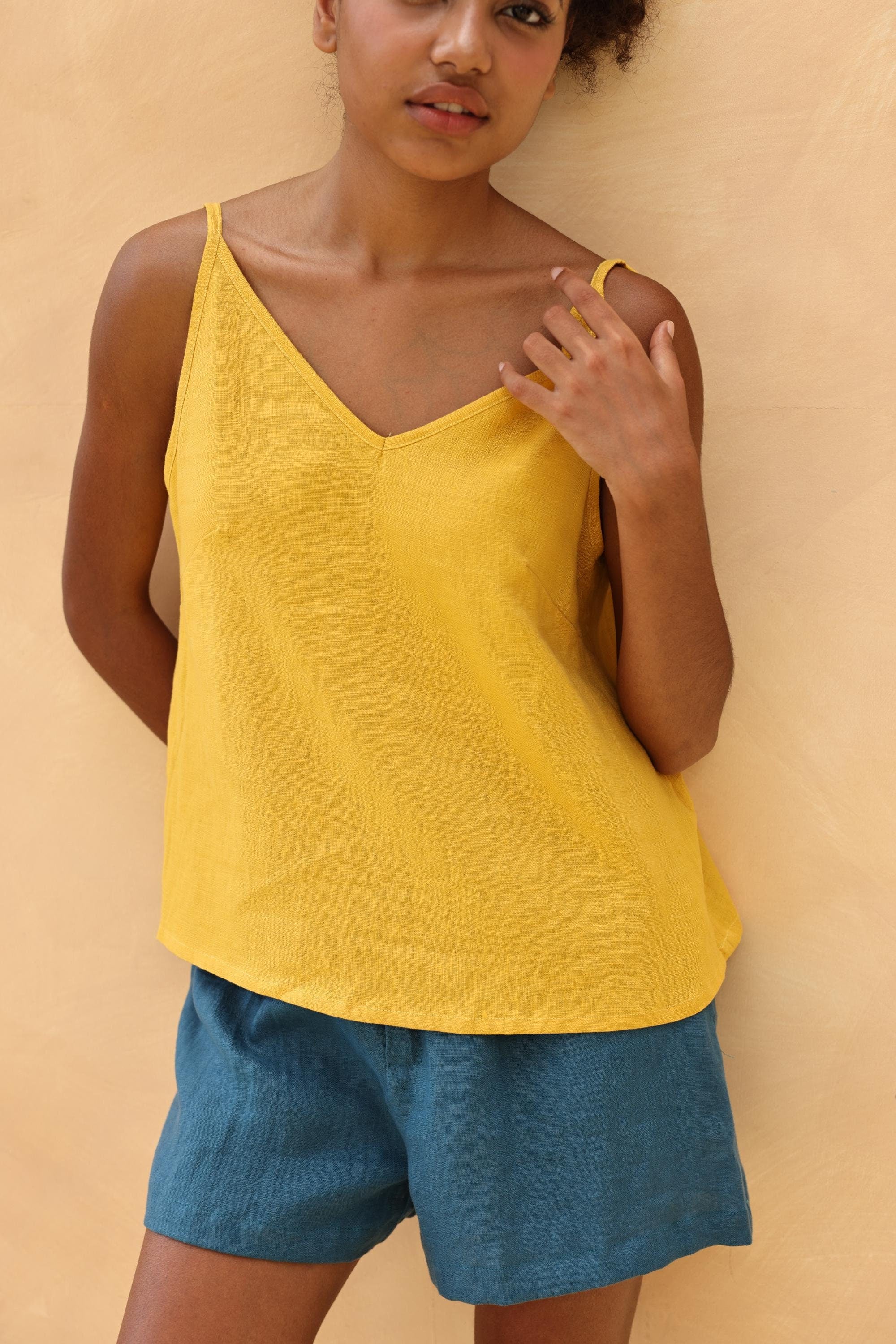 Woman wearing a yellow top and blue shorts against a beige background