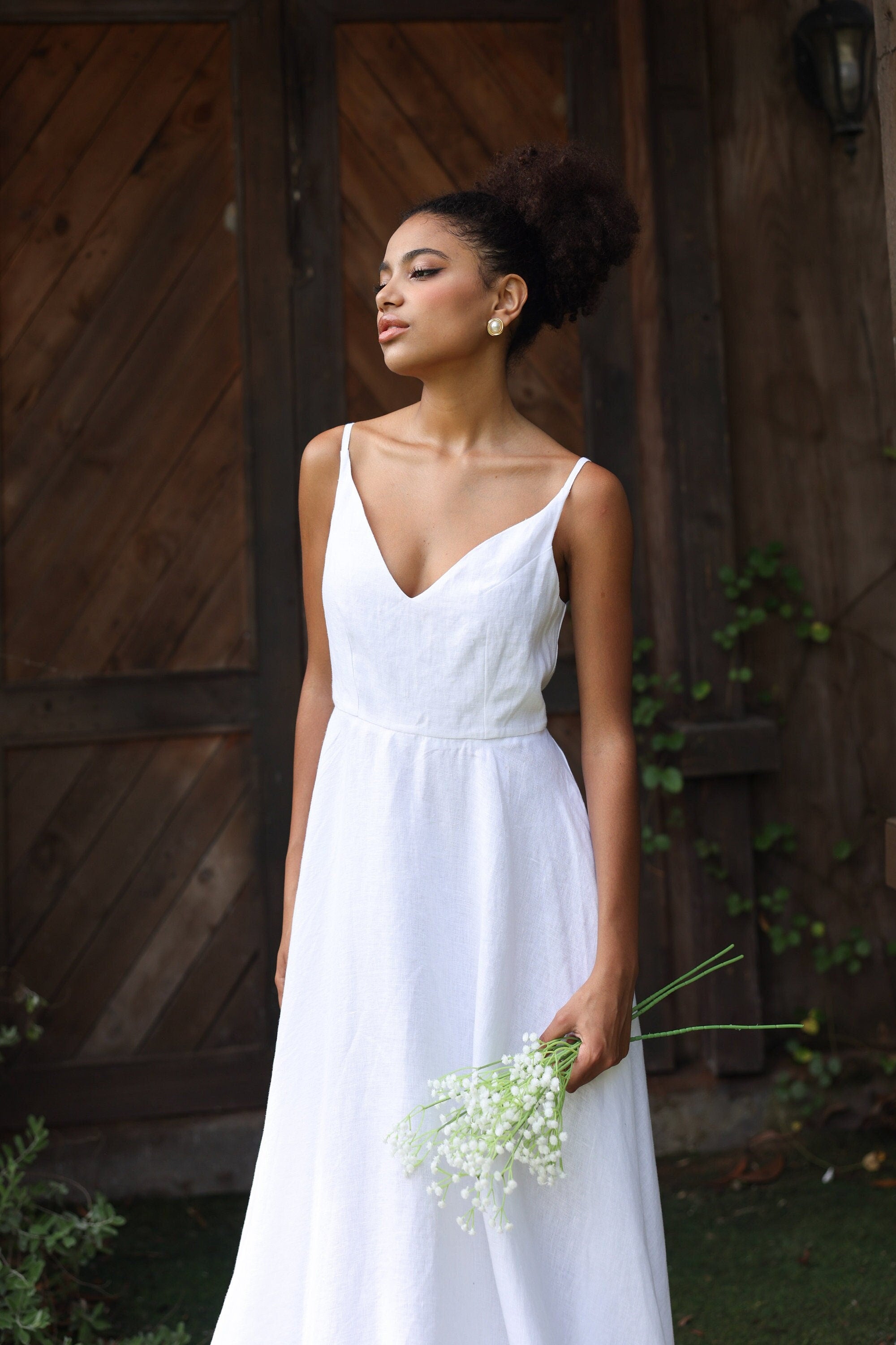 Woman in a white dress holding flowers in front of a wooden door