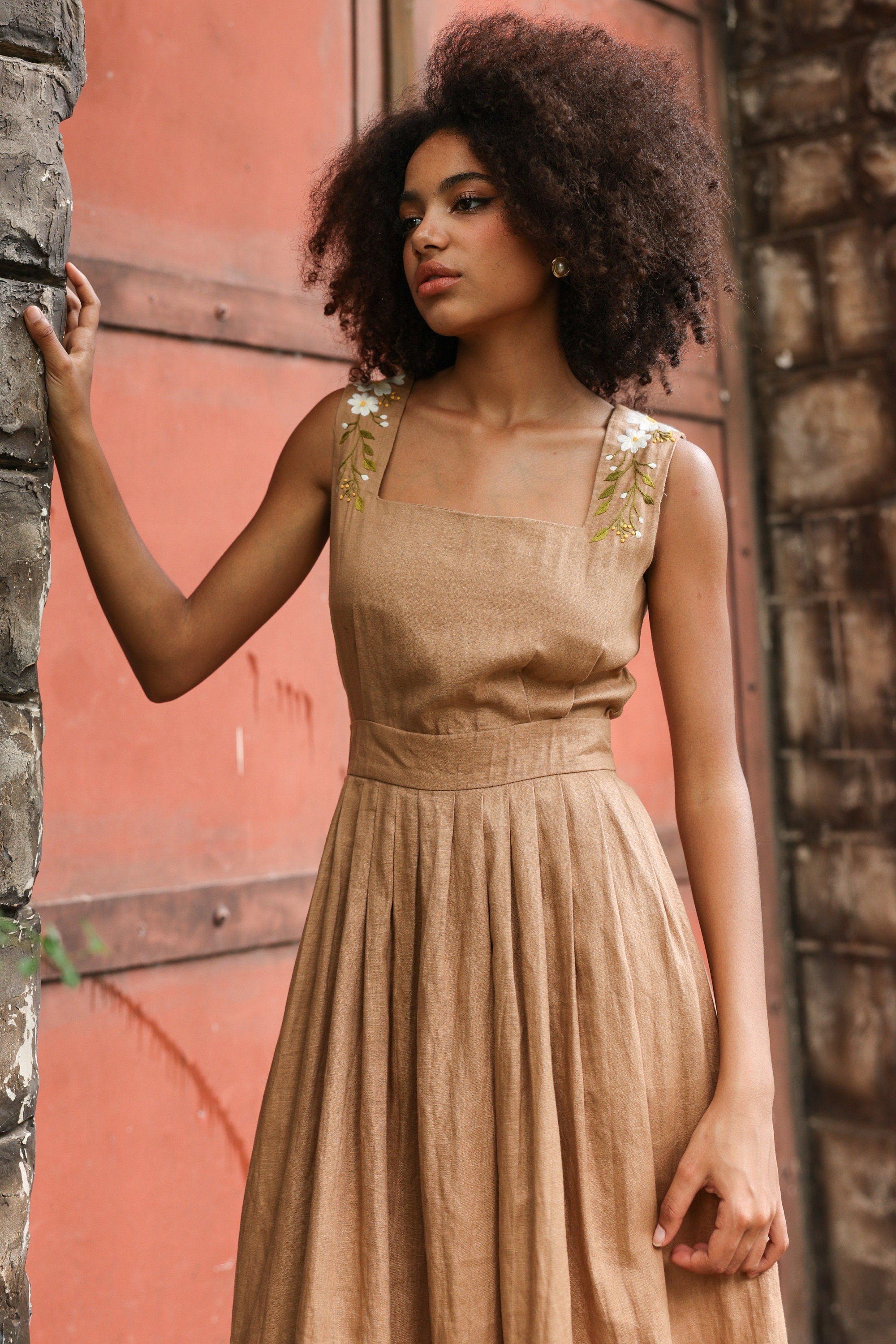 Woman in a dress standing against a textured wall.