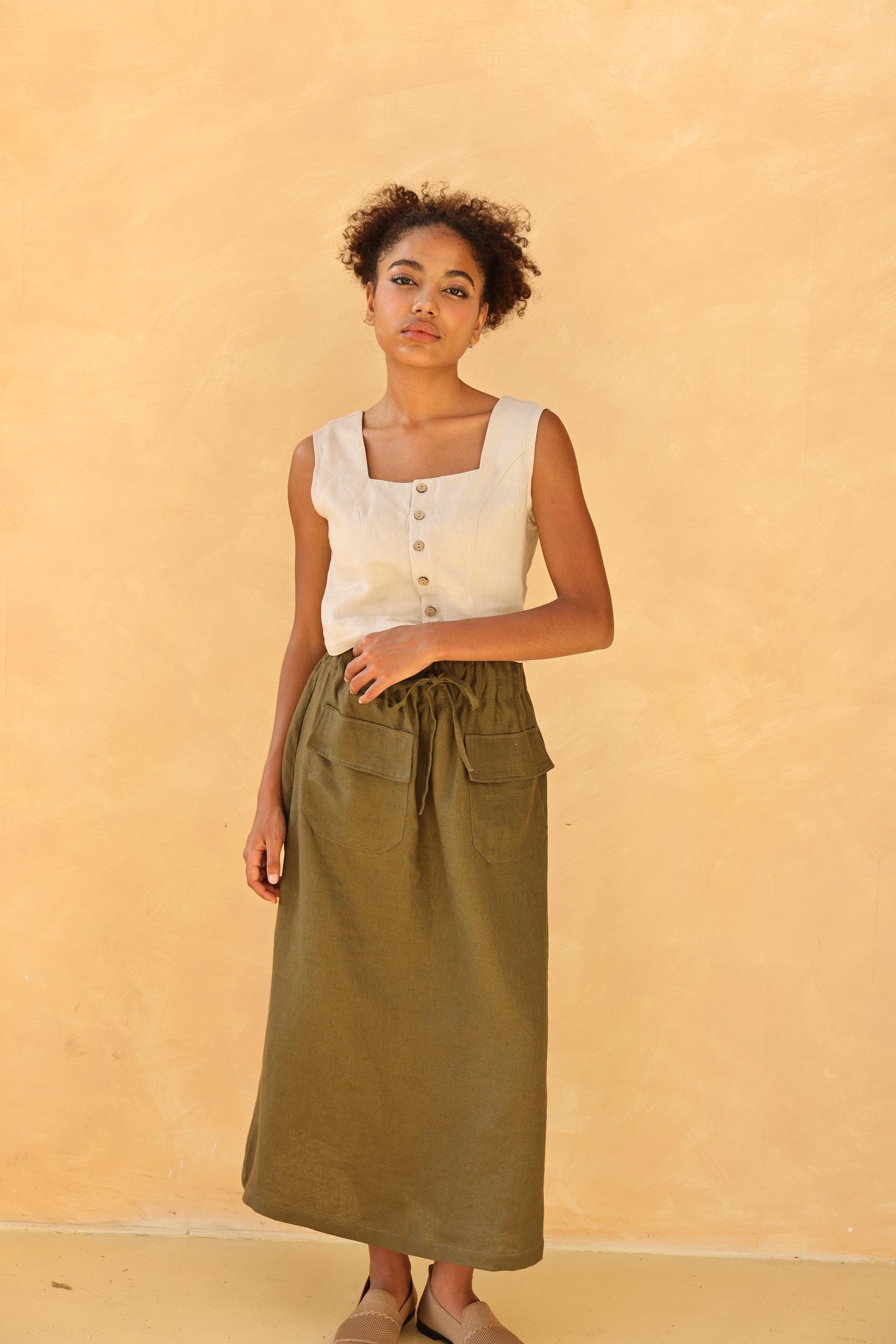 Woman wearing a sleeveless top and green skirt against a beige background