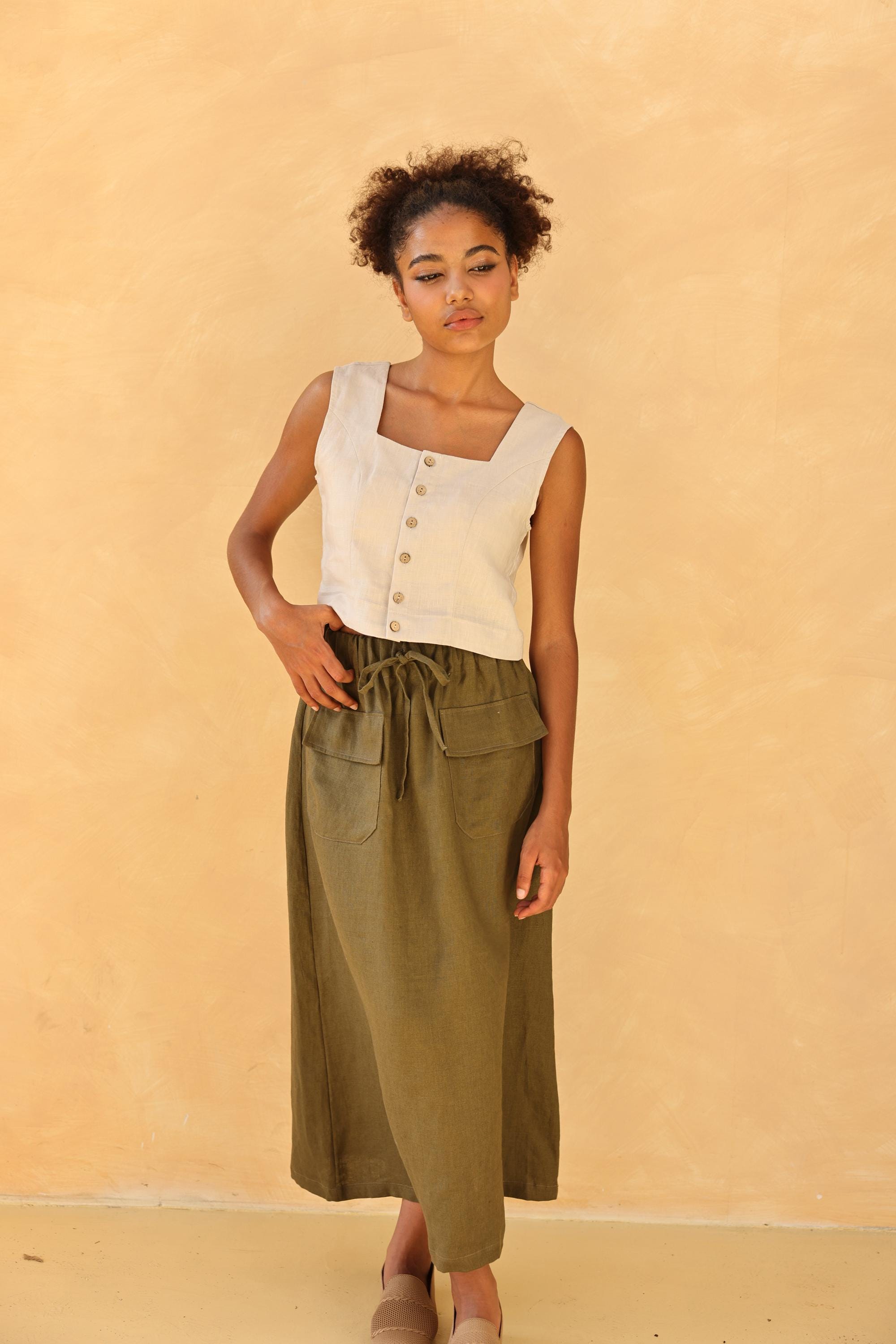 Woman wearing a sleeveless top with buttons and green skirt against a beige background