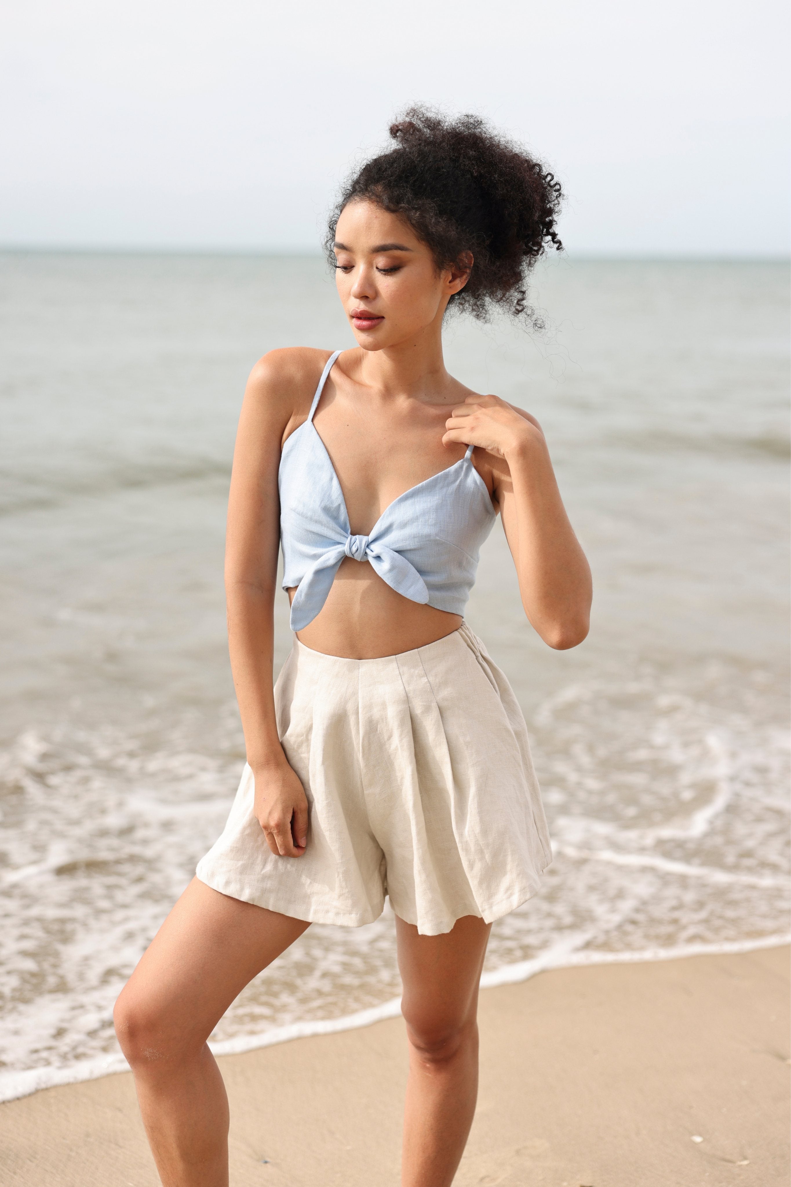 Woman in light blue top and beige shorts standing on a beach