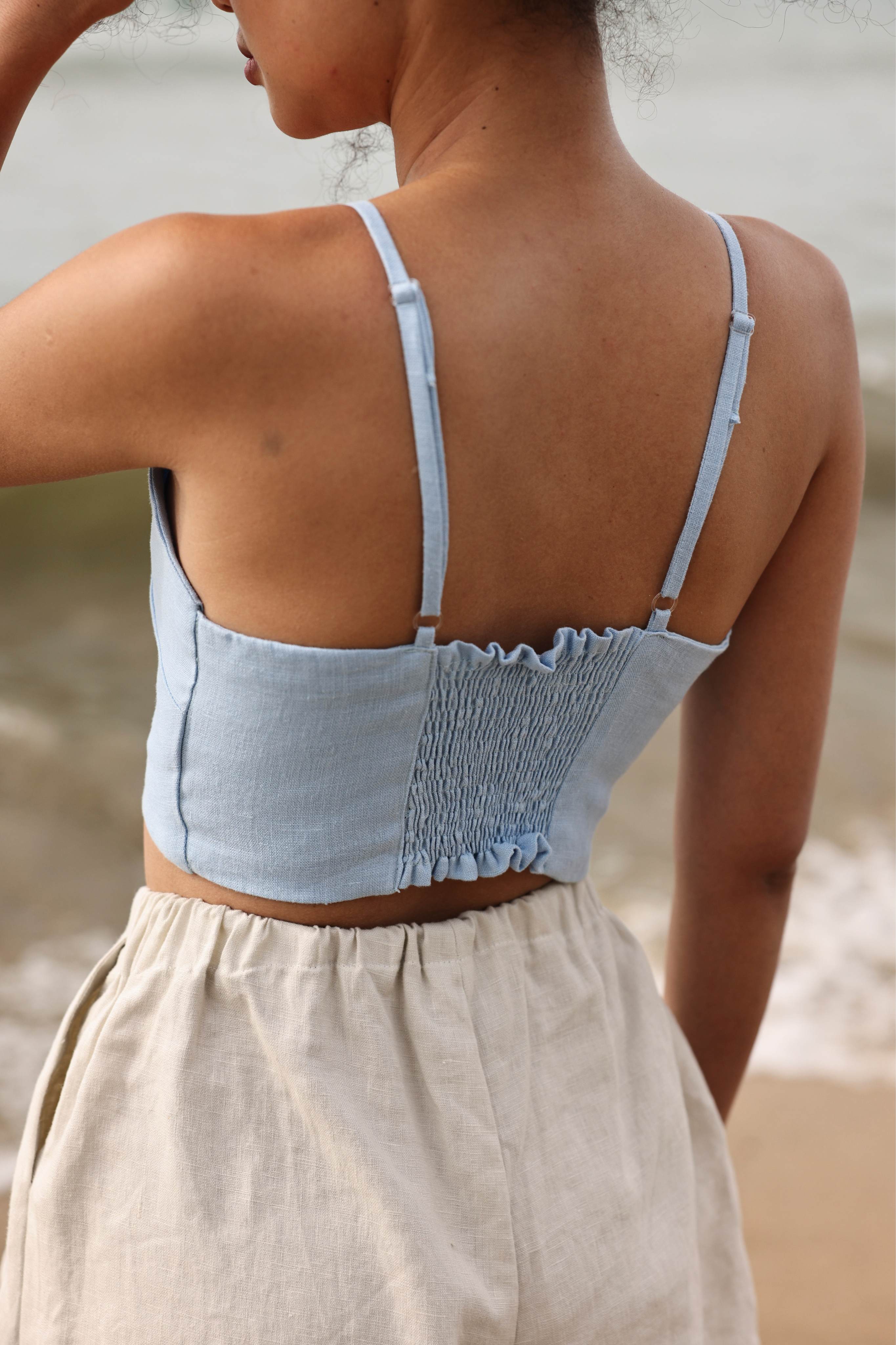 Woman wearing a light blue top and beige shorts on a beach.